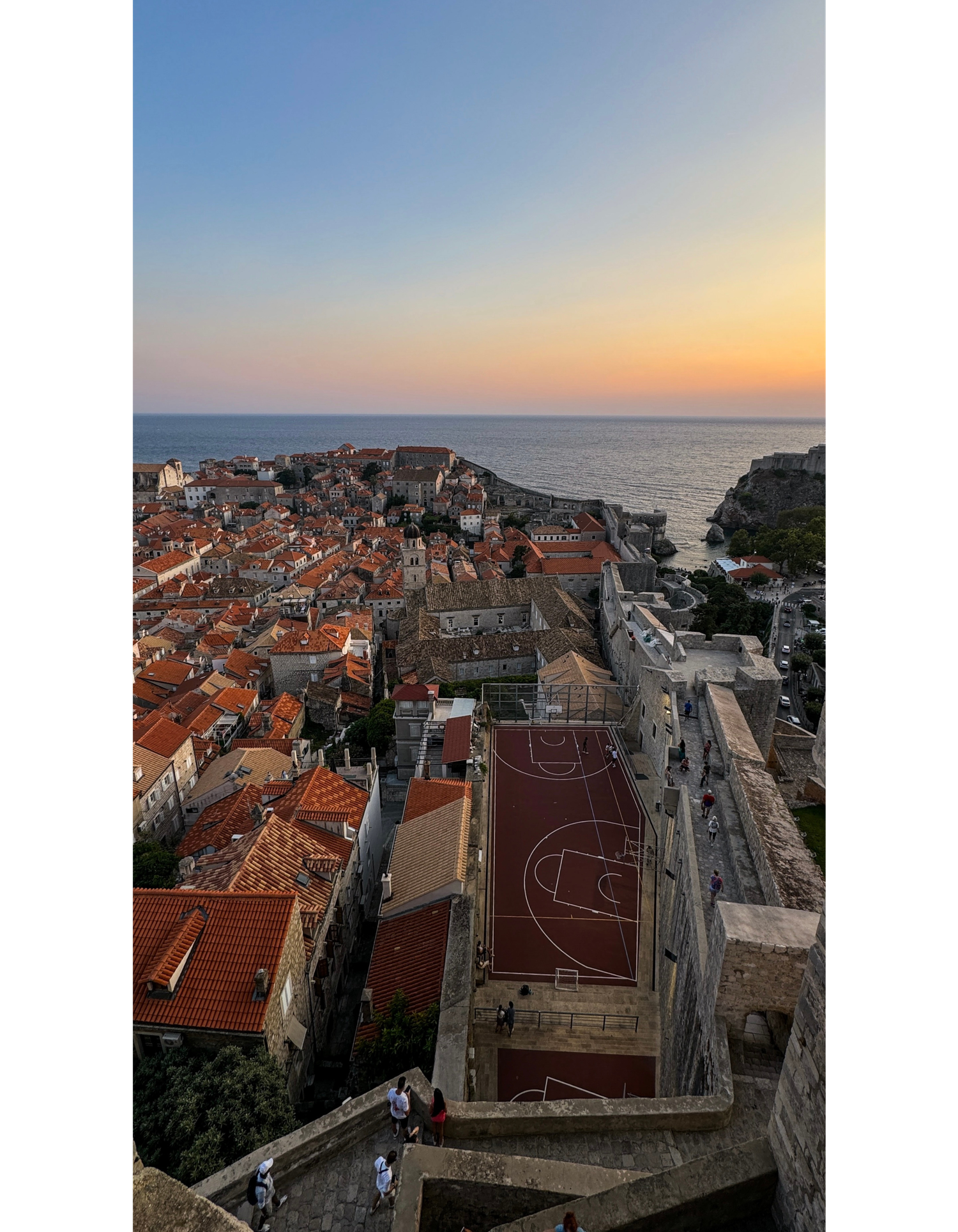 Panoramic sunset view of Dubrovnik's old town with terracotta roofs and basketball court.
