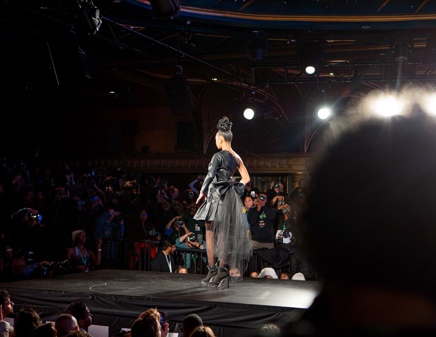 Dark stage with dramatic spotlights illuminating a fashion runway show.