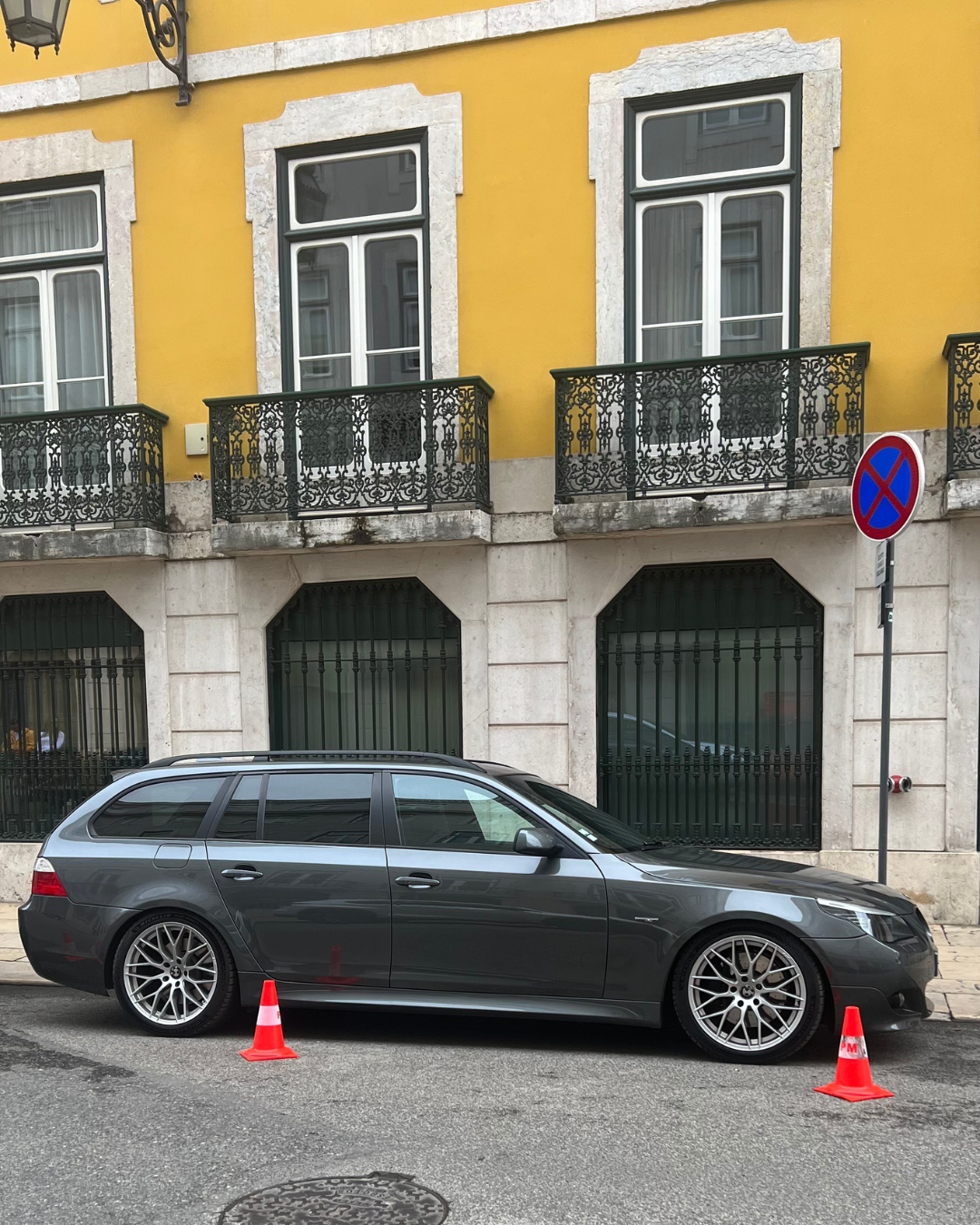 Grey BMW 5-series wagon parked on European street beside yellow building with decorative balconies. Lisbon, Portugal.