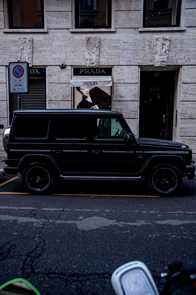 Black luxury SUVs parked in a row along a stone building facade on an urban street.