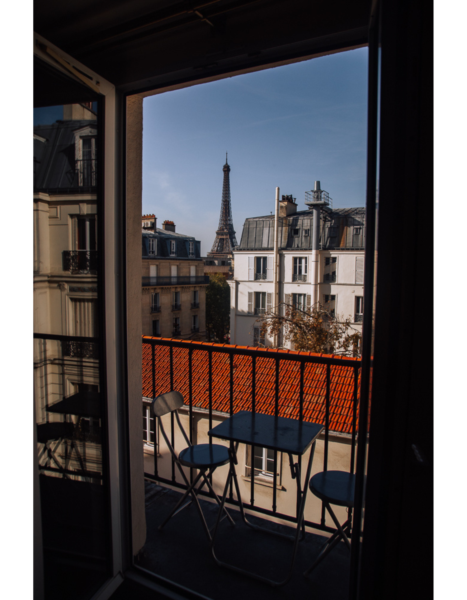 Parisian balcony view featuring the Eiffel Tower visible among classic Haussmanian buildings.