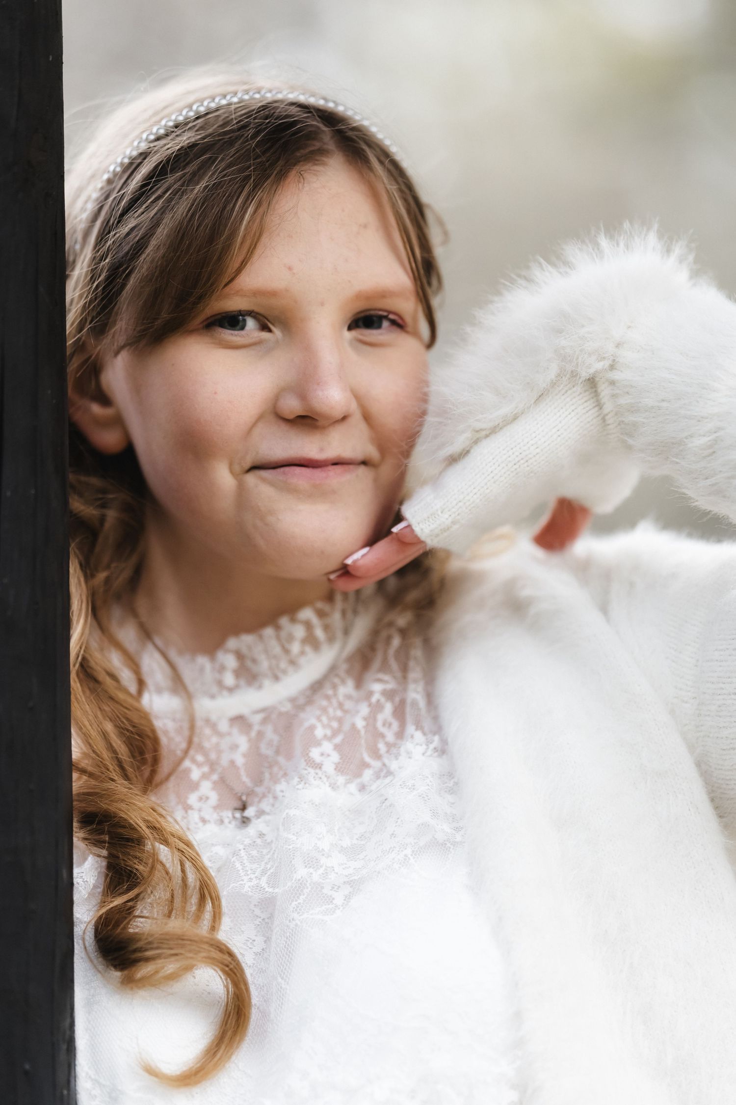 Rippikoulutyttö herkässä kuvassa, karvainen lapanen kädessä ja valkoinen pitsimekko päällä.