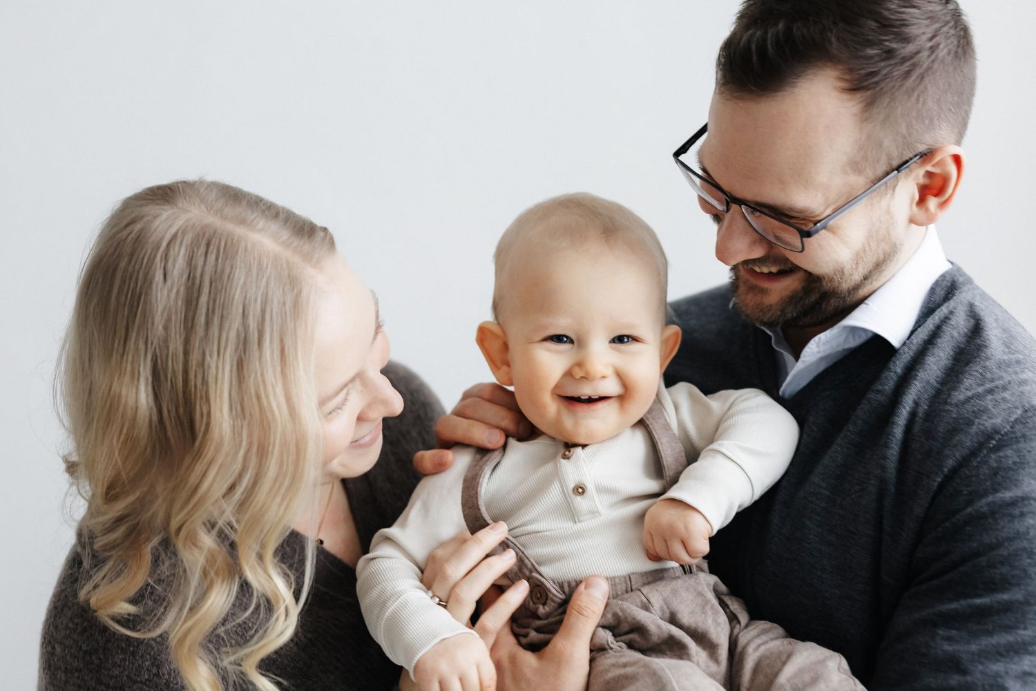 Äiti, lapsi ja isä lähekkäin studiokuvauksessa.