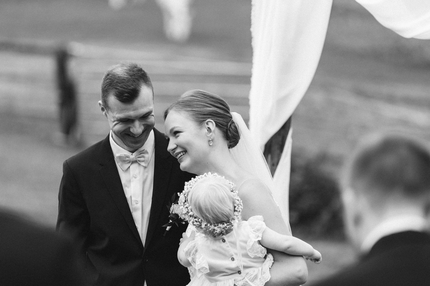 Hymyilevä hääpari alttarilla vihkitilaisuudessa, lapsi sylissään.