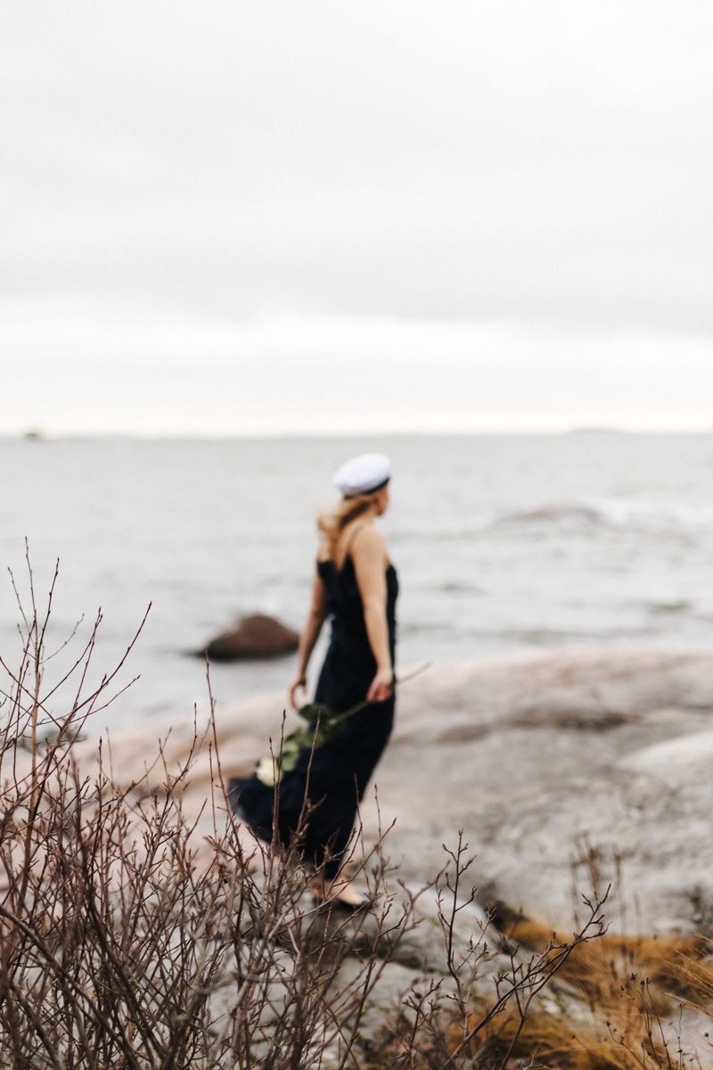 Ylioppilas tuulisella rannalla katsoo merelle päin, hiukset hulmuaa.