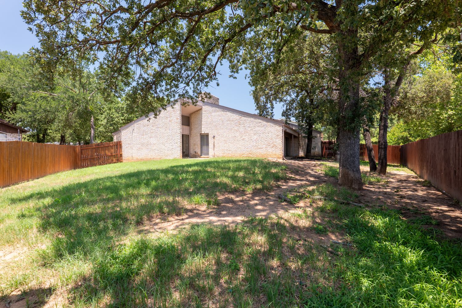 Sloped backyard with established trees and natural landscaping around brick home.