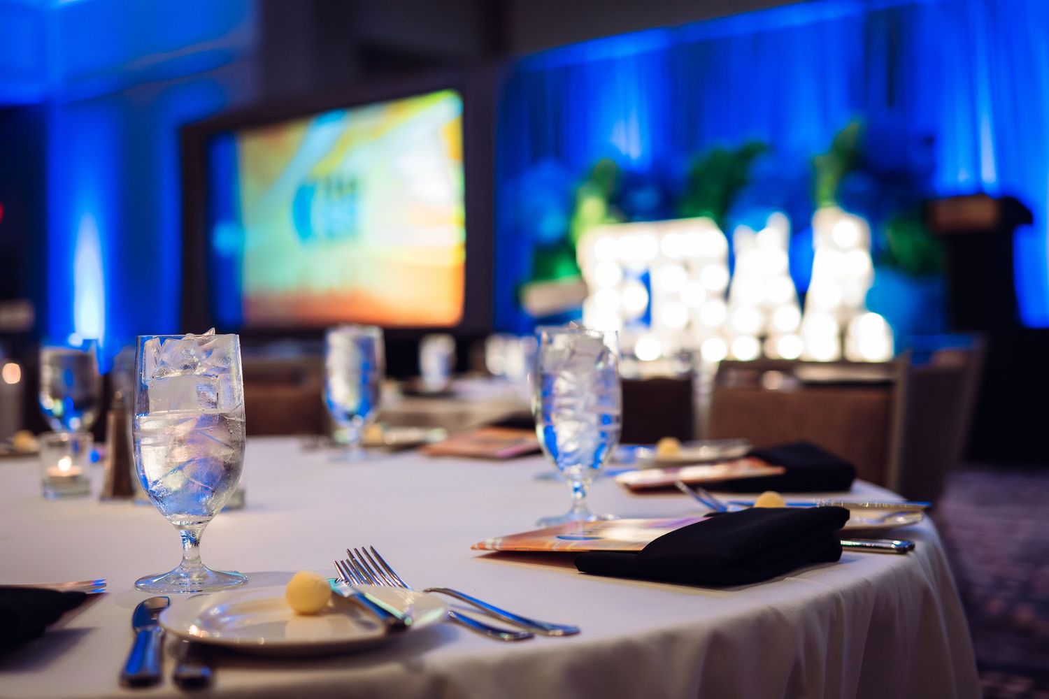Formal dining tables set with blue mood lighting and elegant place settings.