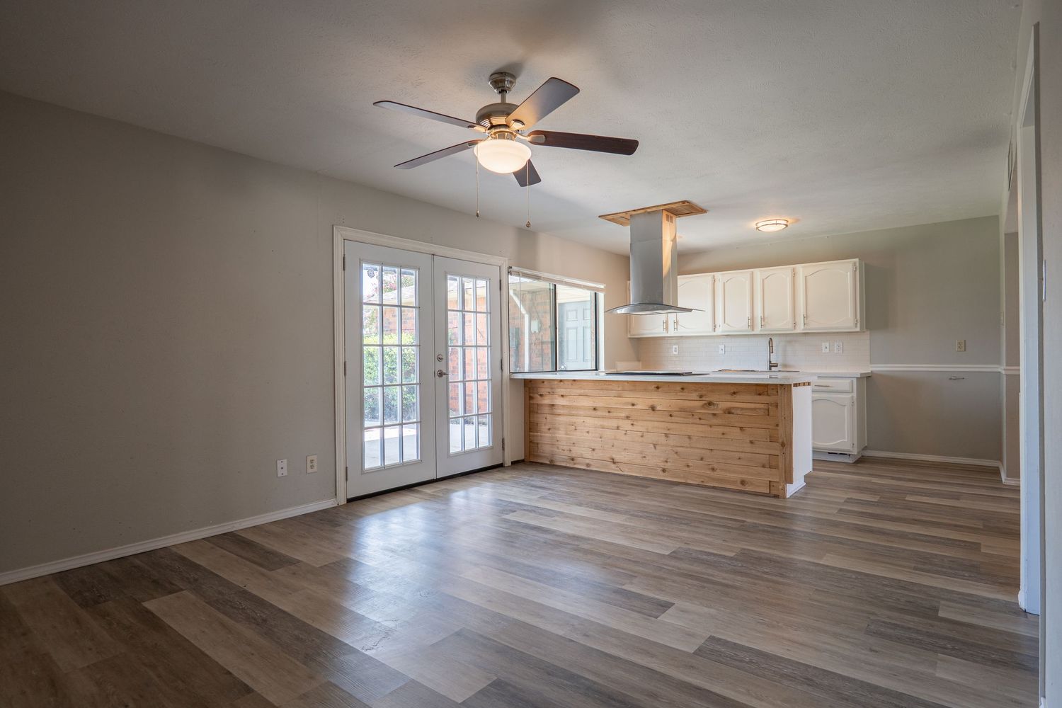Modern open concept living space with hardwood floors, white kitchen cabinets, and ceiling fans in a bright interior.