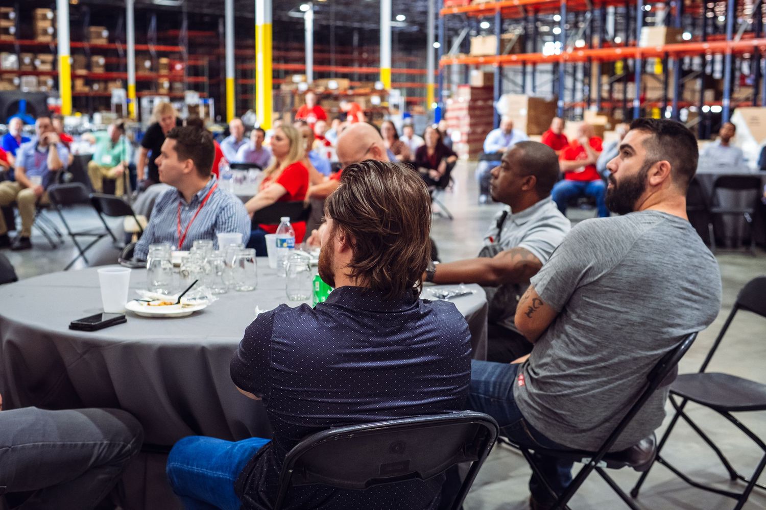 Row of attendees seated in folding chairs at an indoor venue watching presentation.