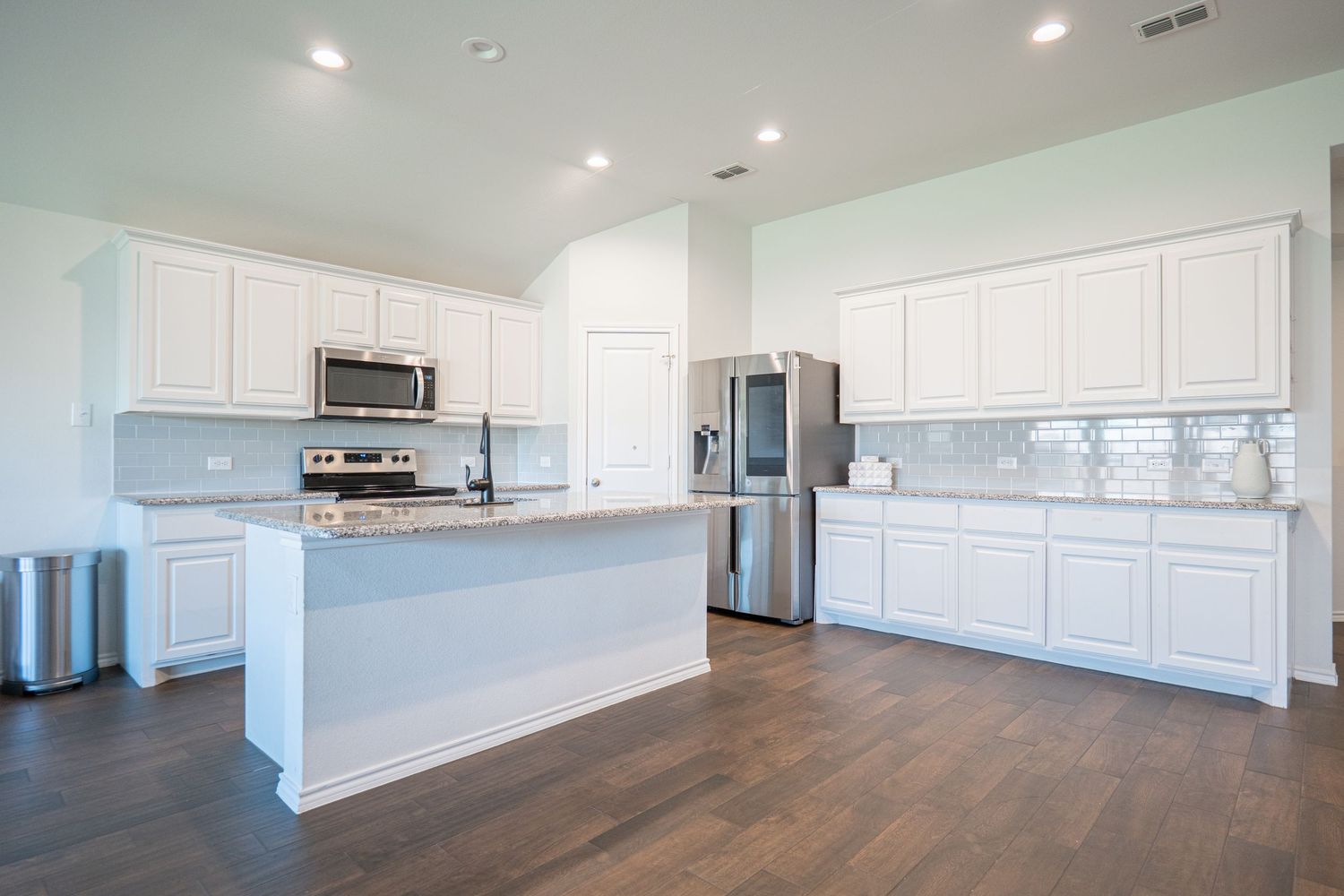 Open concept living space with white kitchen cabinets, hardwood floors and recessed lighting in modern home interior.