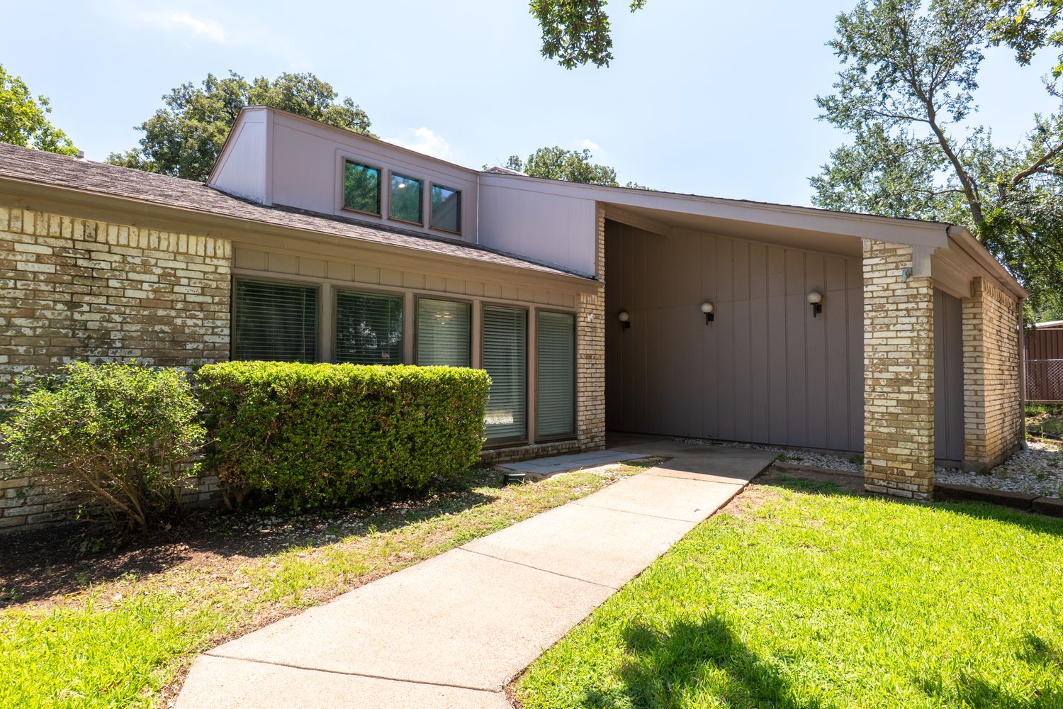 Brick home exterior with wide driveway and established trees providing natural shade.