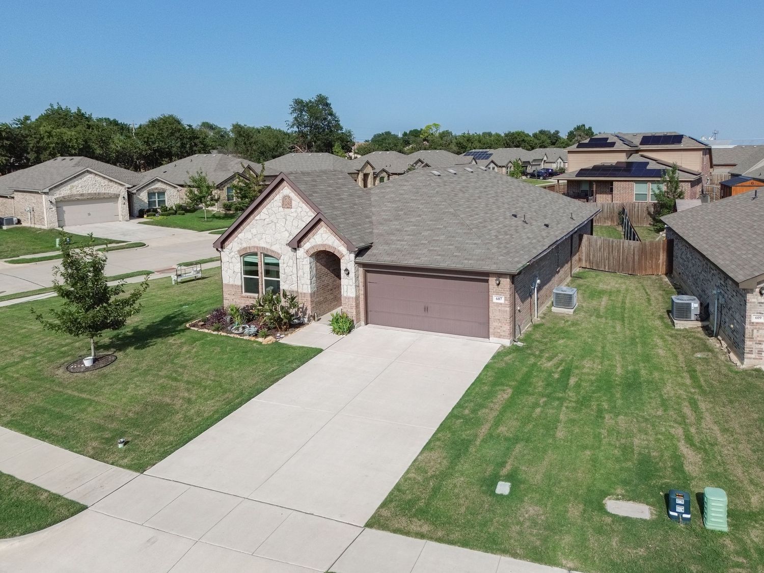Aerial view of suburban homes with well-maintained lawns and tree-lined streets on a sunny day.