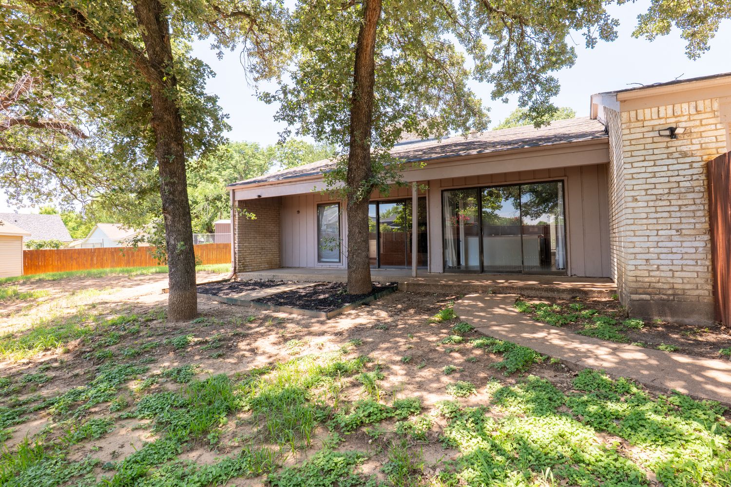 Landscaped backyard with mature trees and brick exterior of residential property.