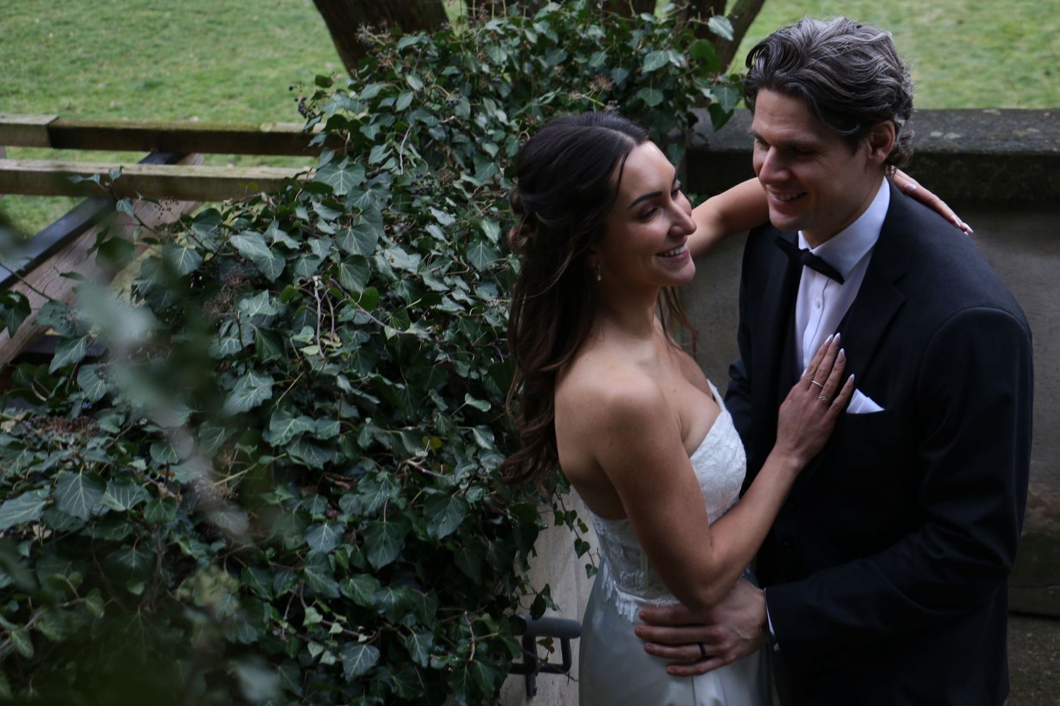 A romantic moment between newlyweds against a lush ivy-covered wall.