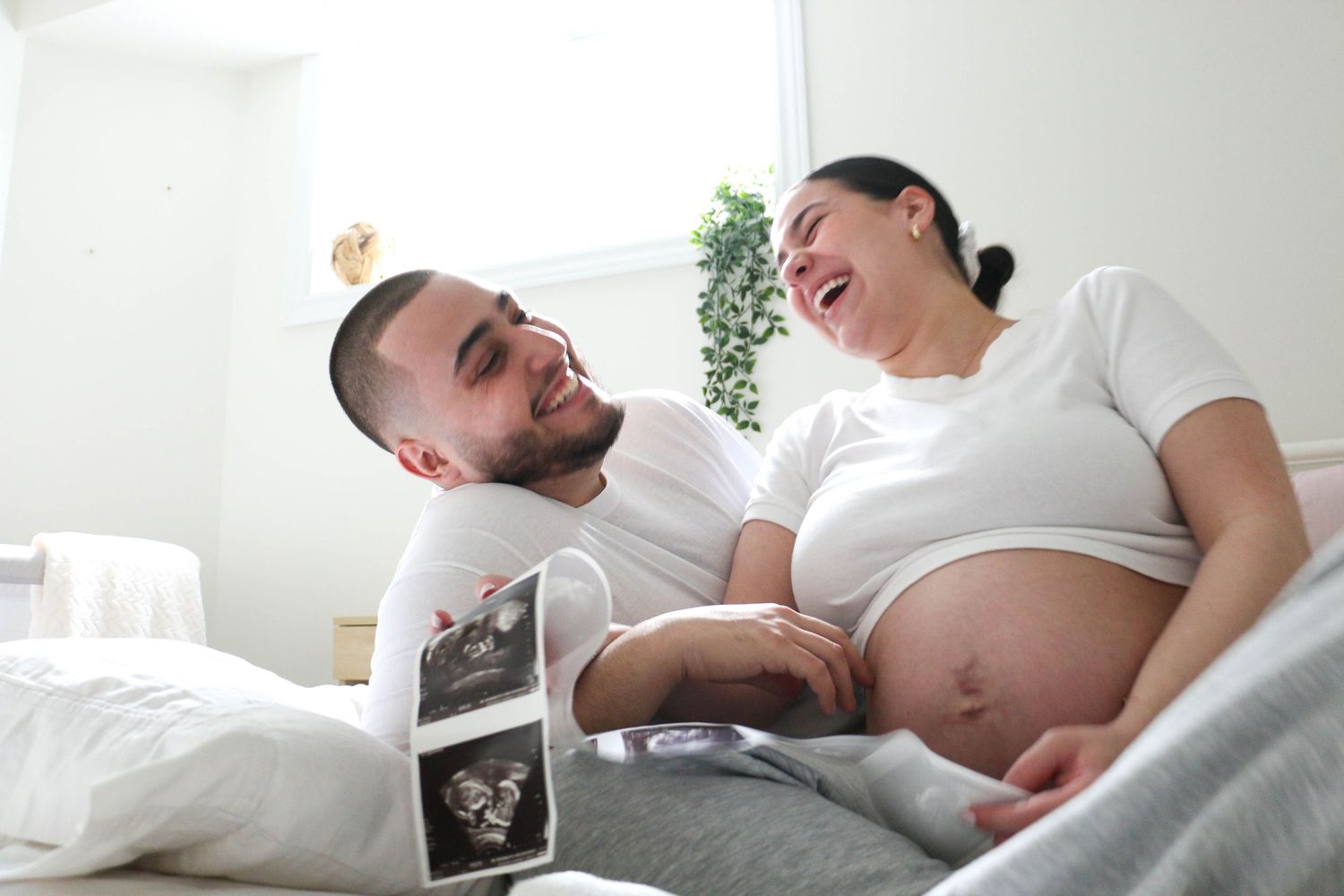 Happy couple shares a tender moment while looking at ultrasound photos in bed.