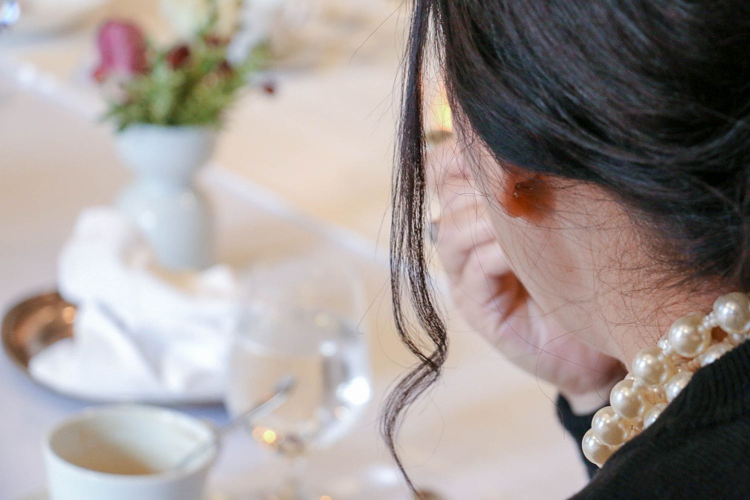 Delicate pearl earrings seen in profile at an elegant dining setting.