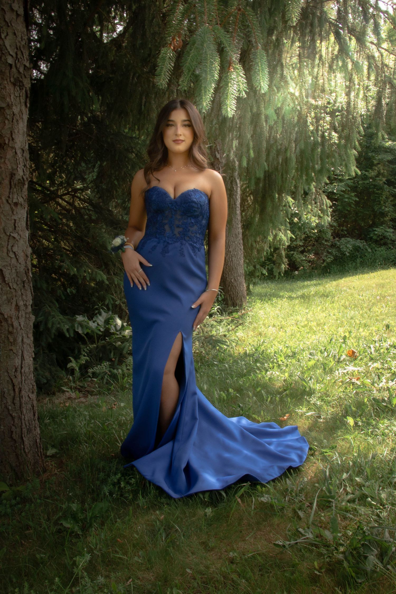 A stunning royal blue evening gown with a sweetheart neckline and flowing train photographed in a forest setting.