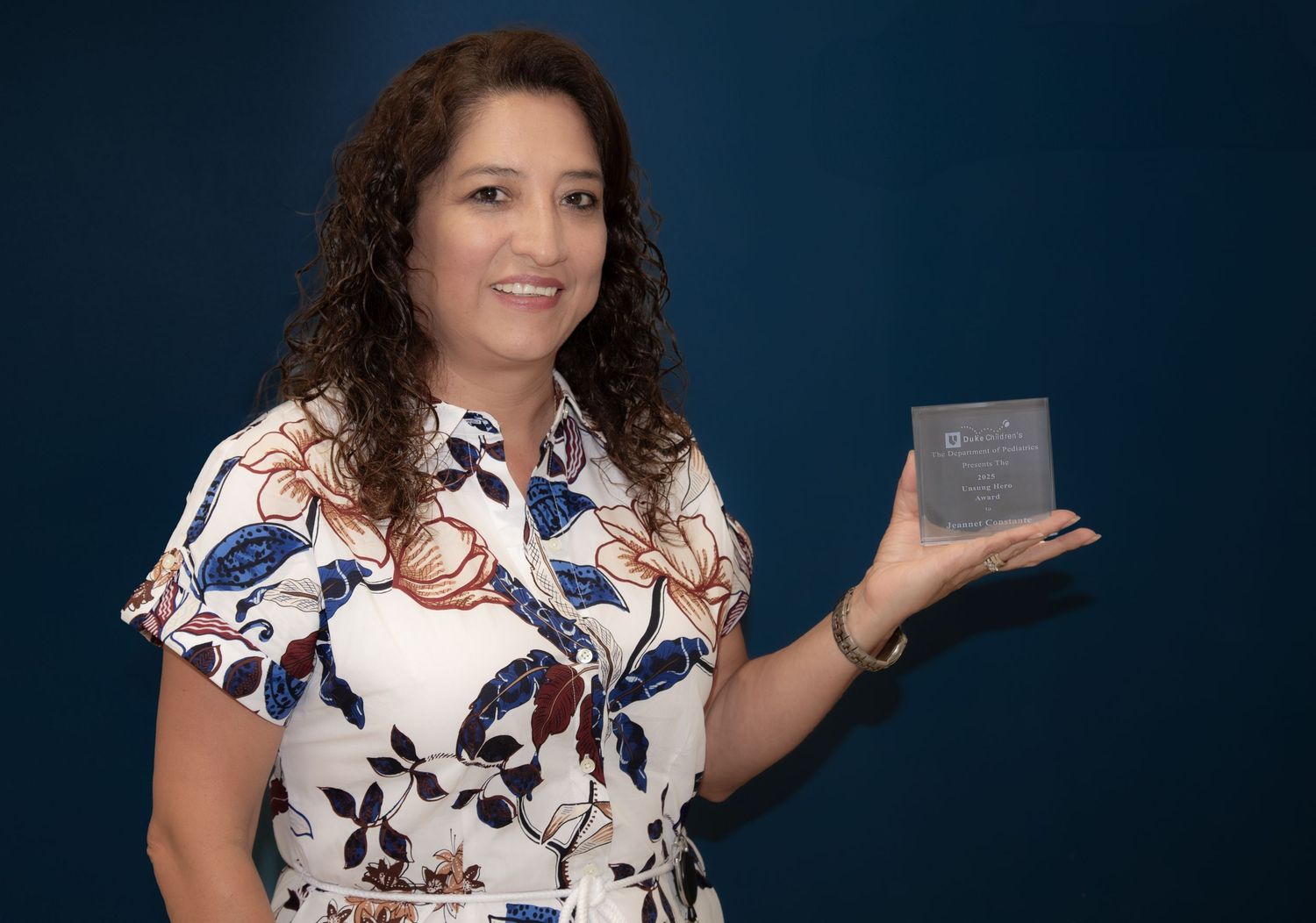 Smiling woman holding a work recognition award during an office celebration.