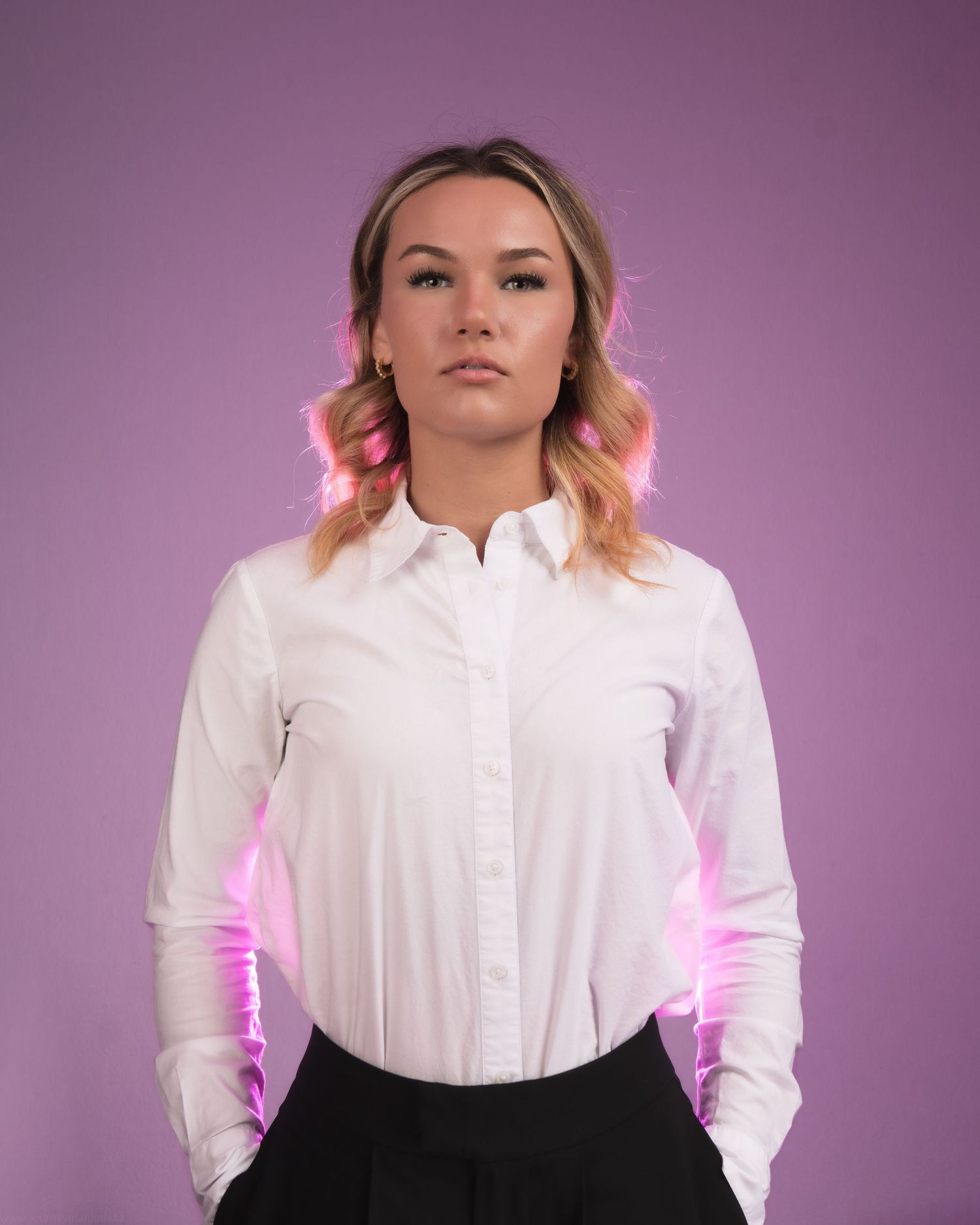 Young woman in white button-up shirt poses against purple background with pink neon lighting accents.