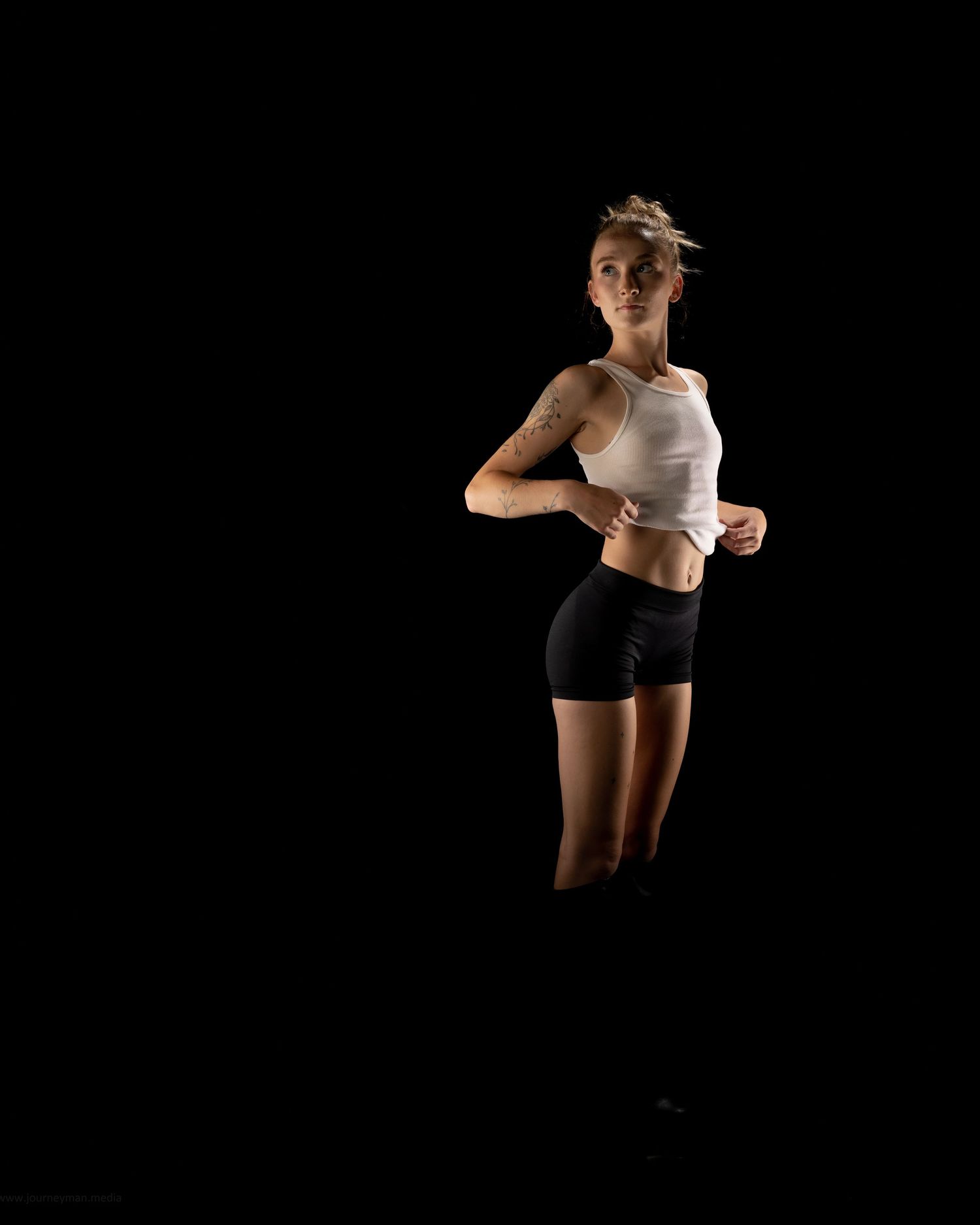 Athletic figure in black shorts and white top performing dynamic leaps against dark backdrop.