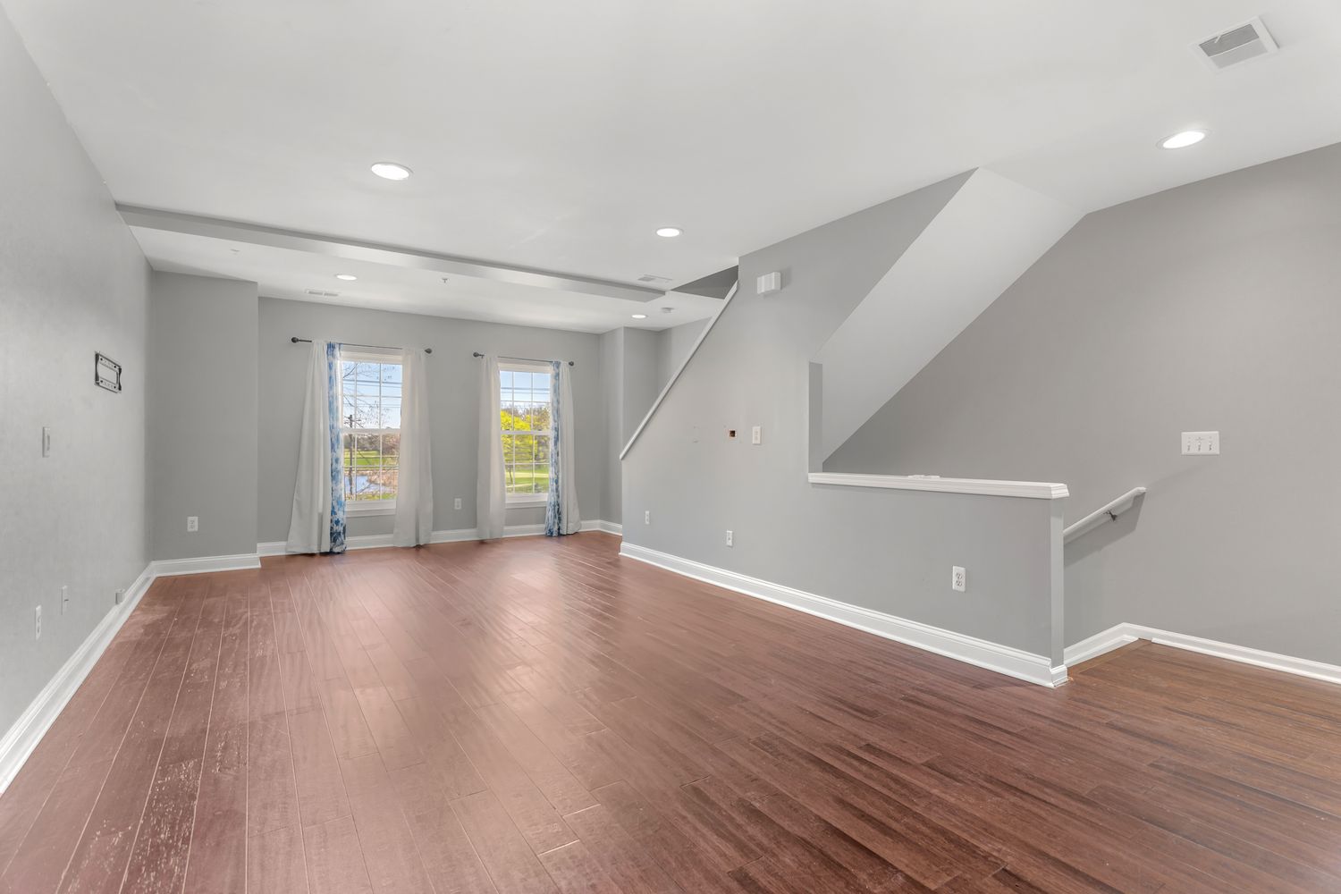 Spacious basement recreation room with grey walls, recessed lighting and hardwood flooring.