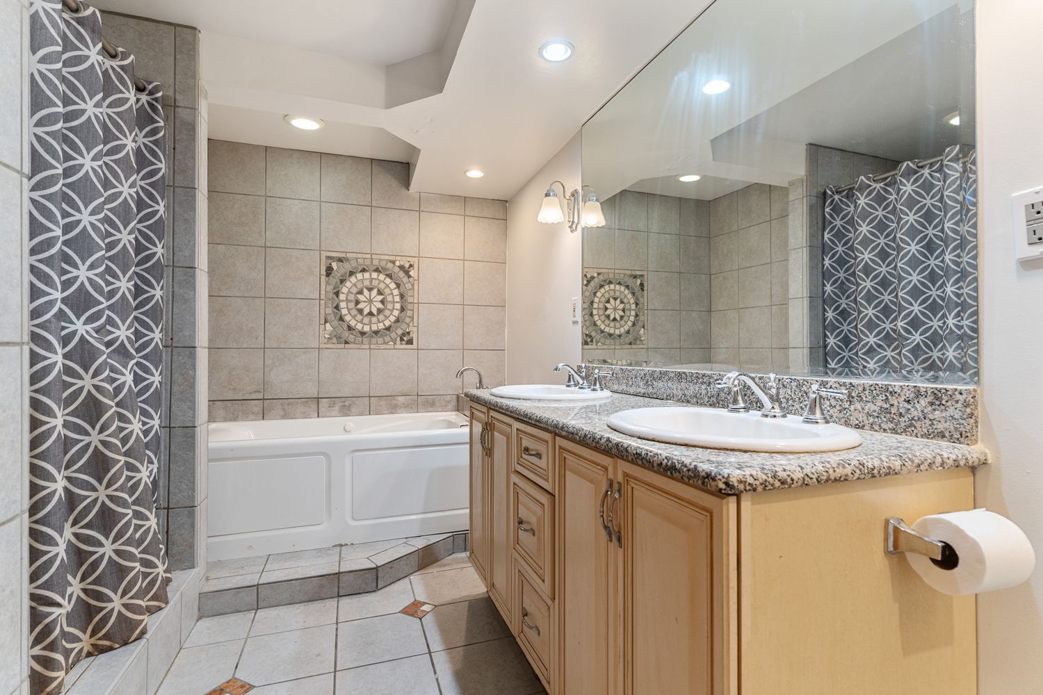 Contemporary bathroom with geometric tile pattern and light wood vanity cabinets.