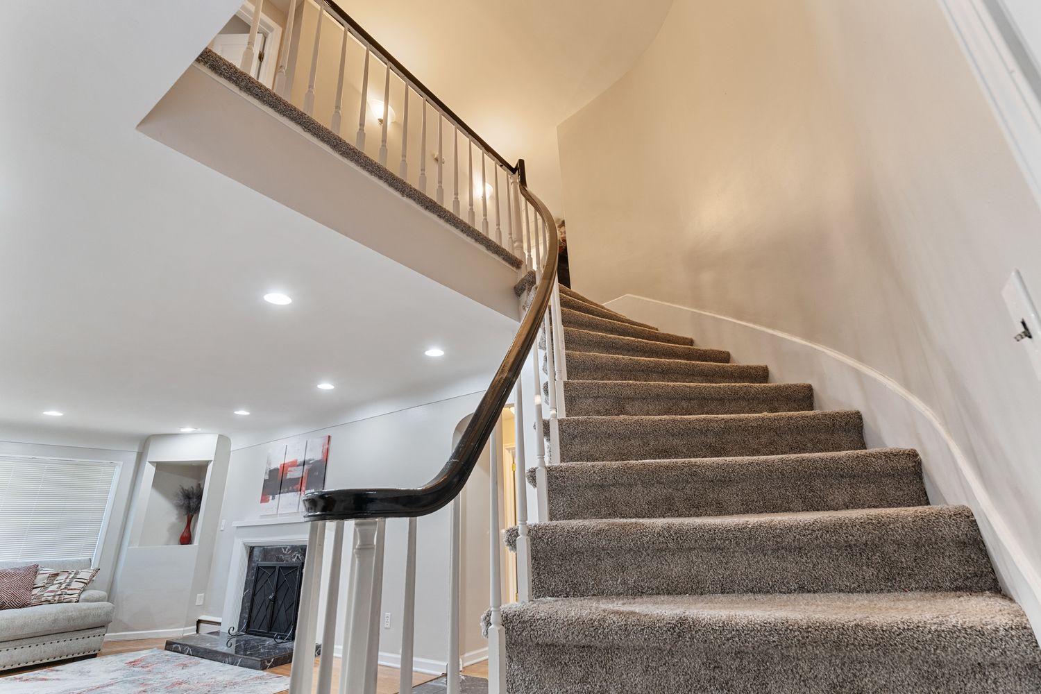 Carpeted staircase with white walls and recessed lighting leading to upper level.