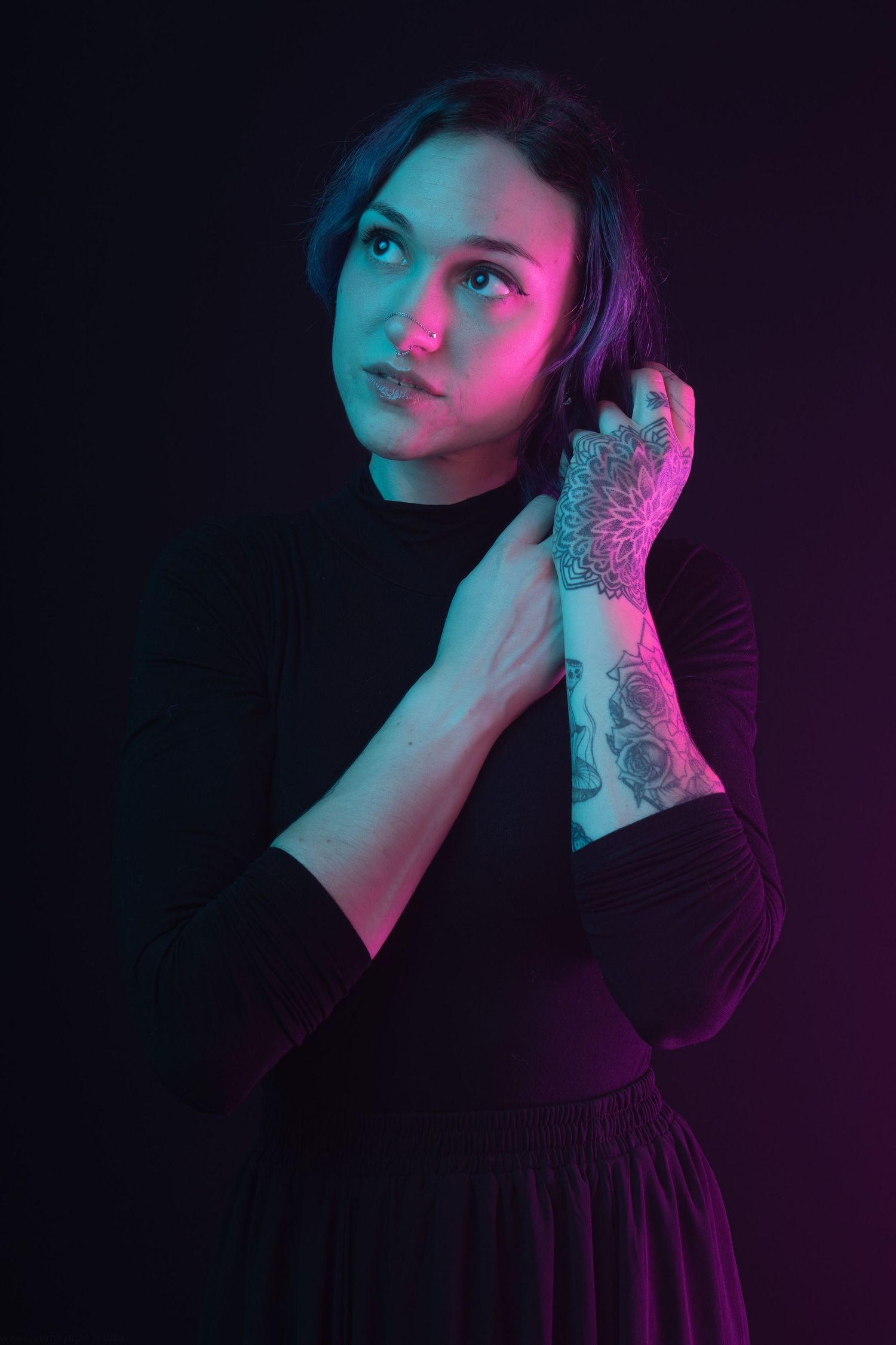 Woman with hand tattoo posing in dramatic pink and teal neon lighting against dark background.