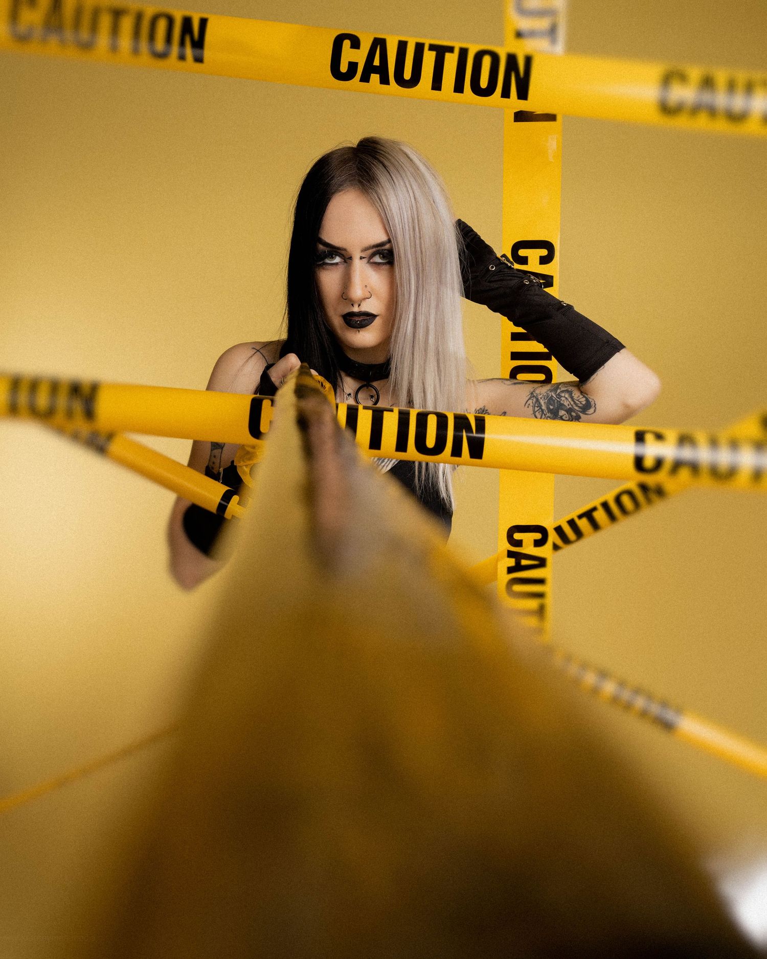 Gothic woman with dark makeup surrounded by yellow caution tape against a golden background.