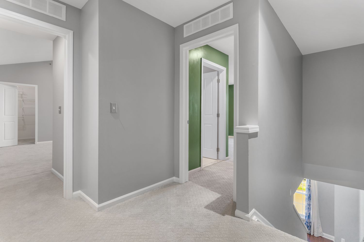 Hallway view showing multiple doorways and neutral grey walls with modern lighting fixtures.