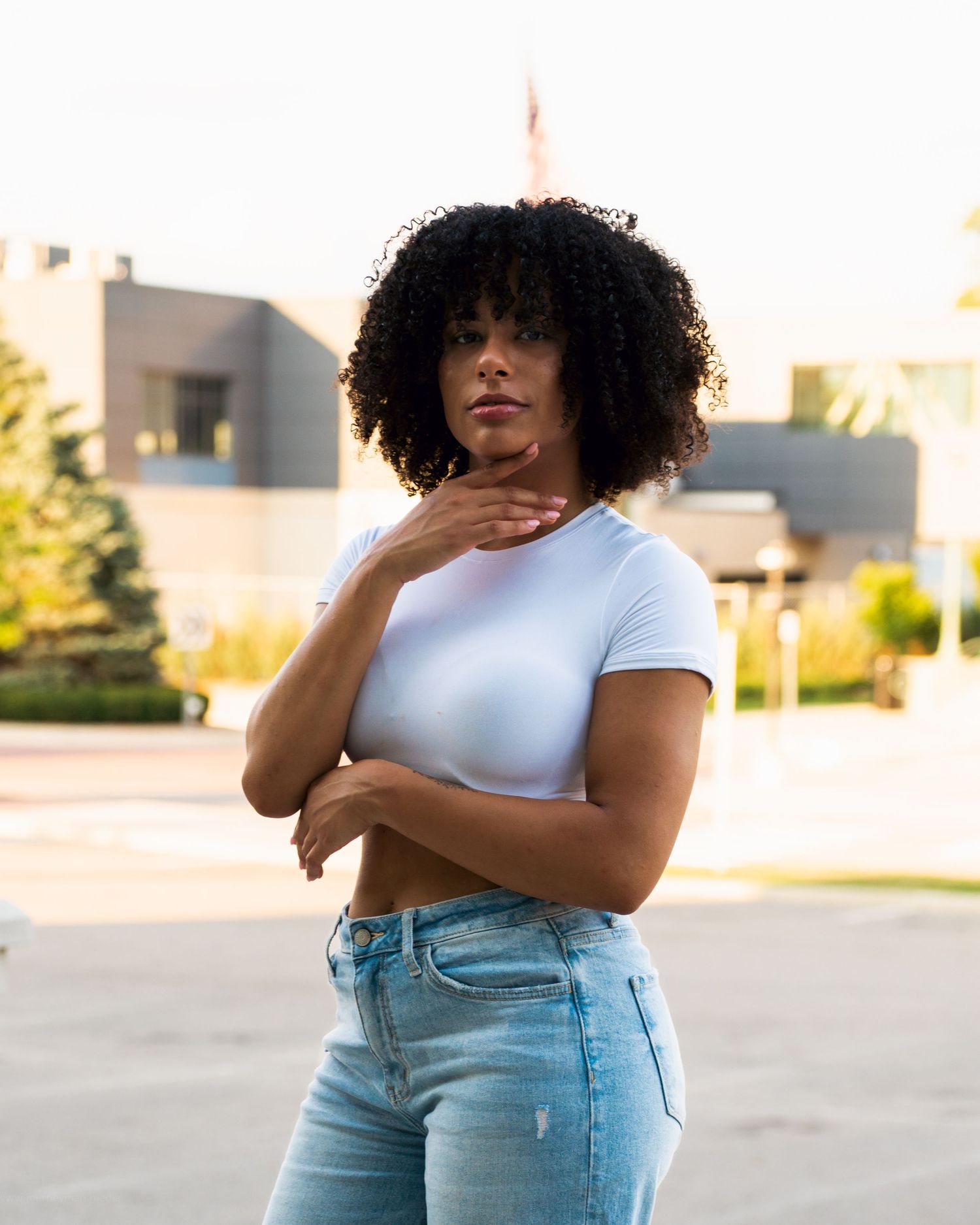 Casual figure poses expressively in ripped blue jeans and white t-shirt against an urban outdoor backdrop.