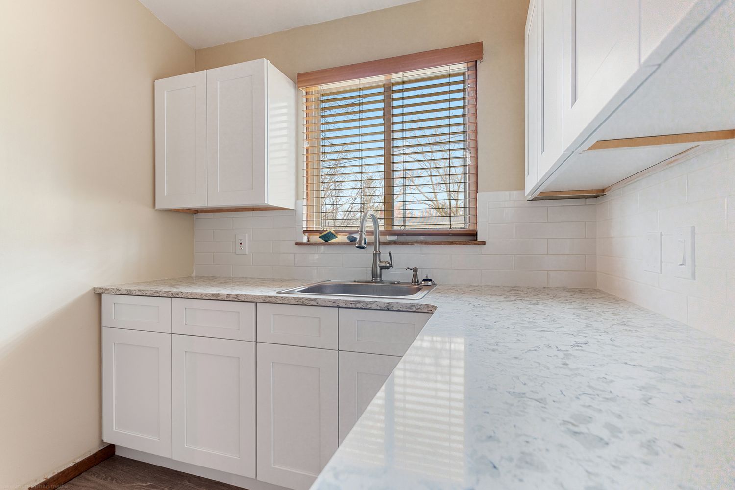 Contemporary white kitchen with marble countertops and large windows in natural lighting.