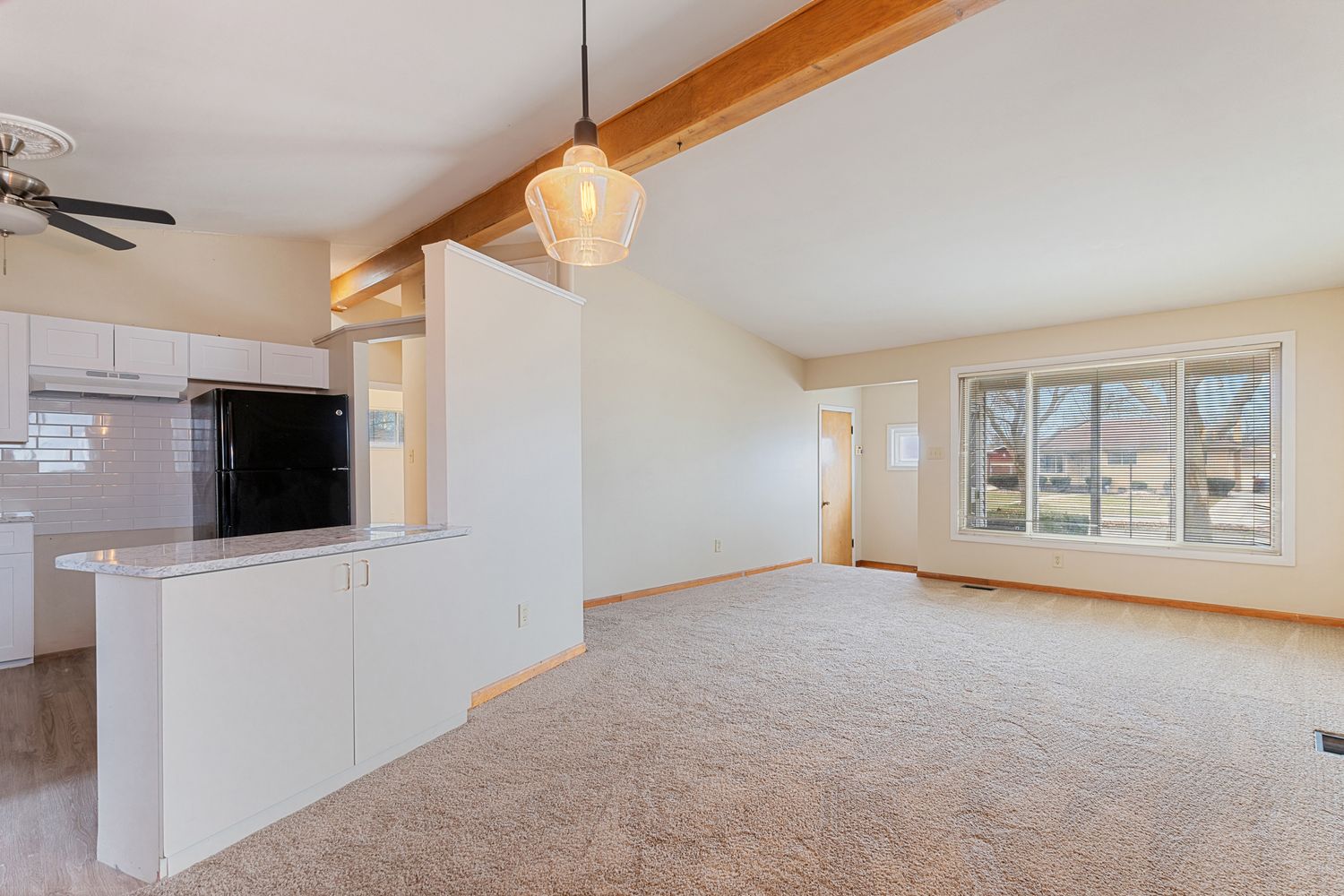 Modern open concept living room interior with exposed wooden beams and recessed lighting.