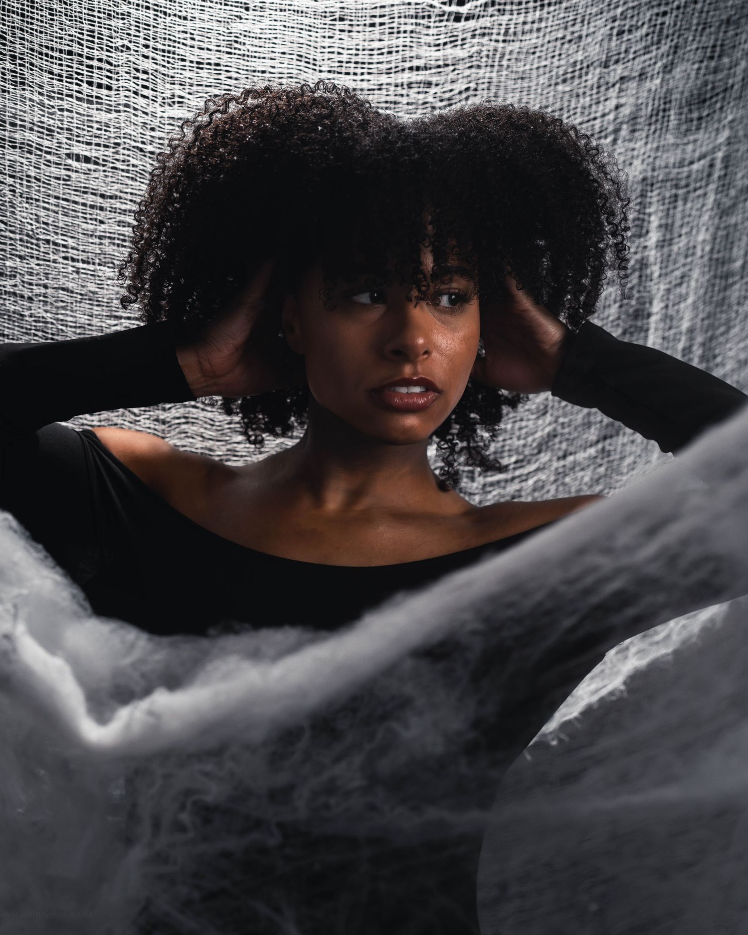 Artistic portrait showing curly hair and soft fabric in moody lighting with dramatic shadows.