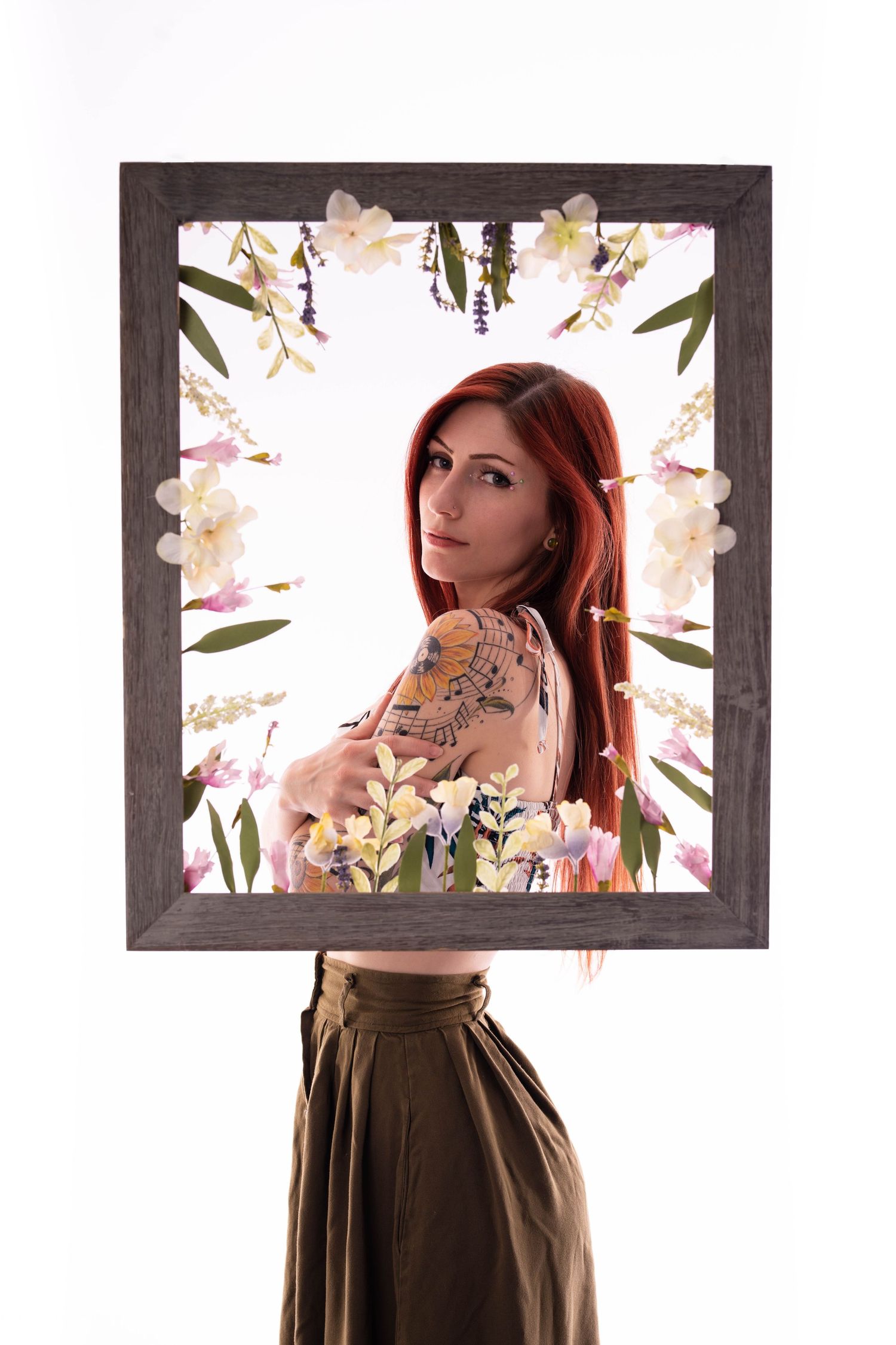 Red-haired tattooed woman posing behind a decorative wooden frame adorned with colorful spring flowers.