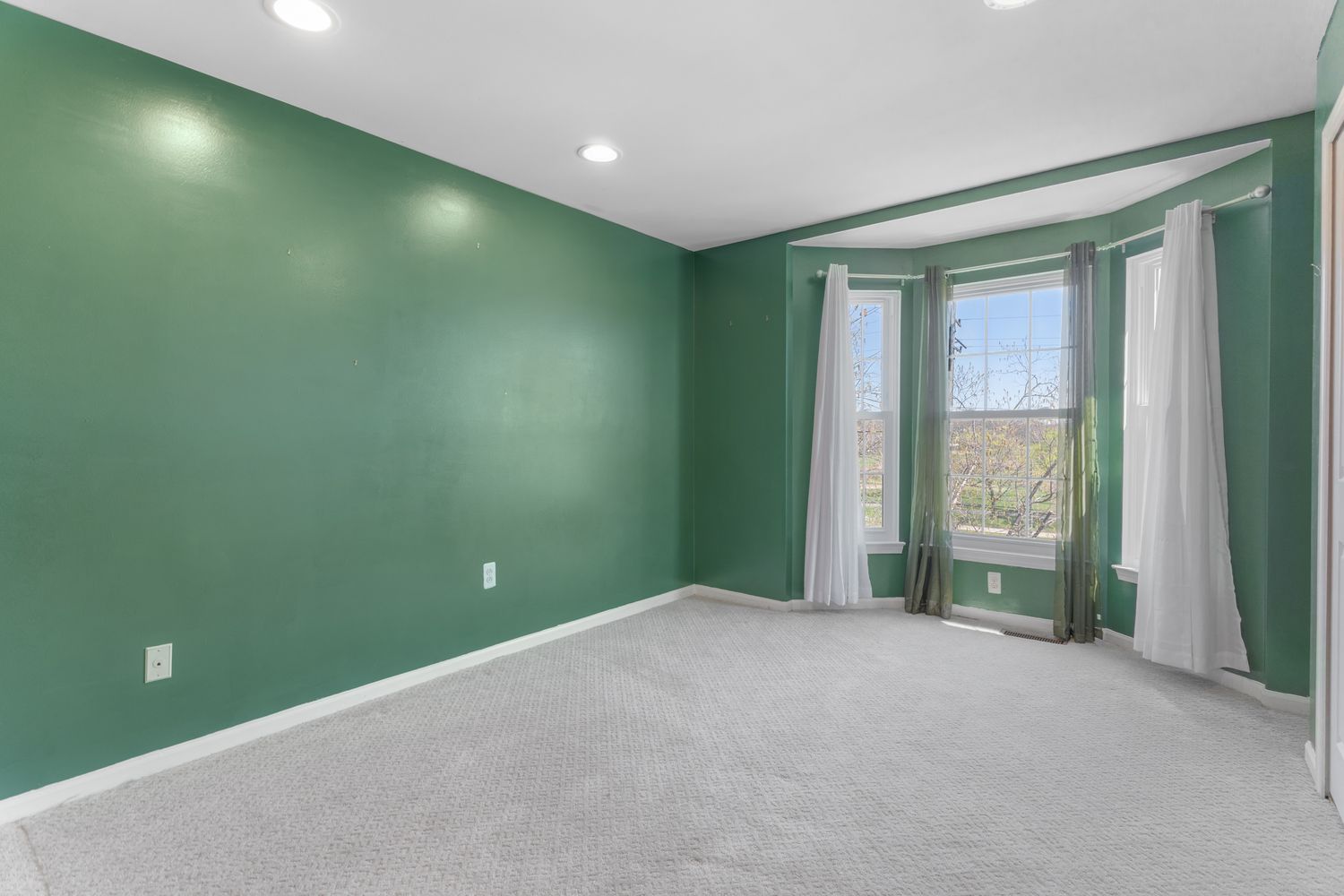 Large room with bold green walls, white trim and natural lighting.