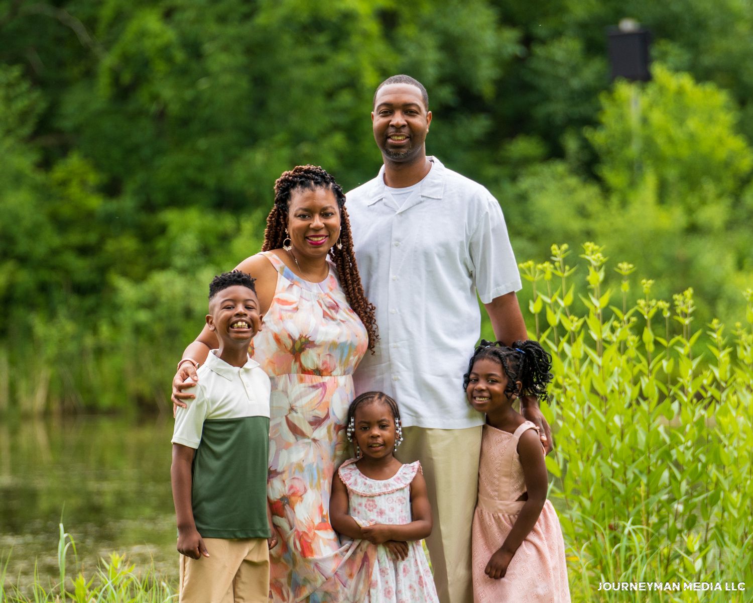 A loving family stands together outdoors surrounded by lush green vegetation on a sunny summer day.