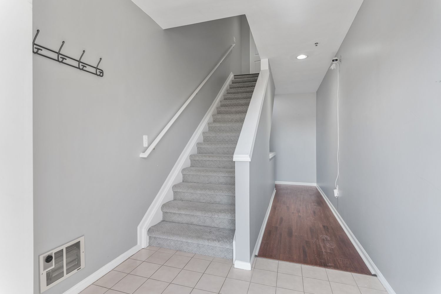Modern interior hallway with white walls, wood flooring and recessed lighting leading to a staircase.