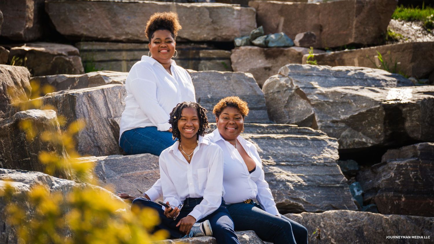 Family sits together on natural stone steps surrounded by autumn foliage during an outdoor photo session.