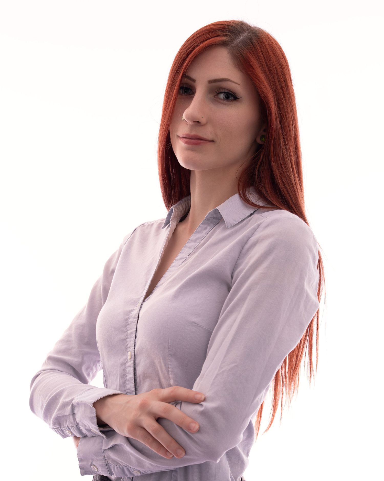 Professional woman with long red hair in white button-up shirt standing with arms crossed against white background.