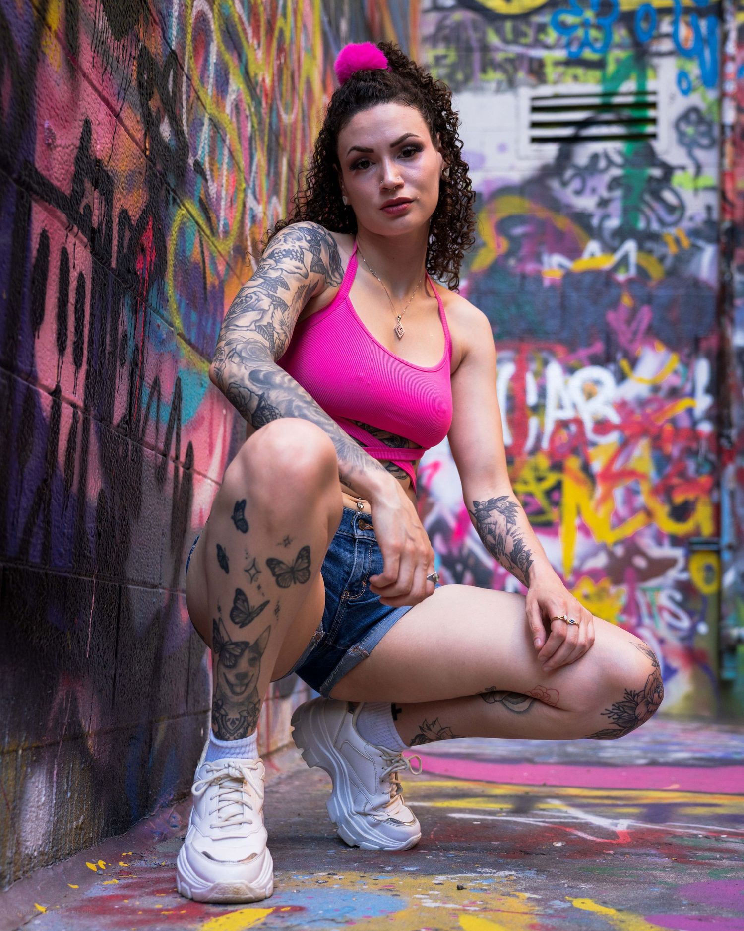 Athletic figure posing dynamically against colorful graffiti wall in urban dance sequence wearing pink top and denim shorts.