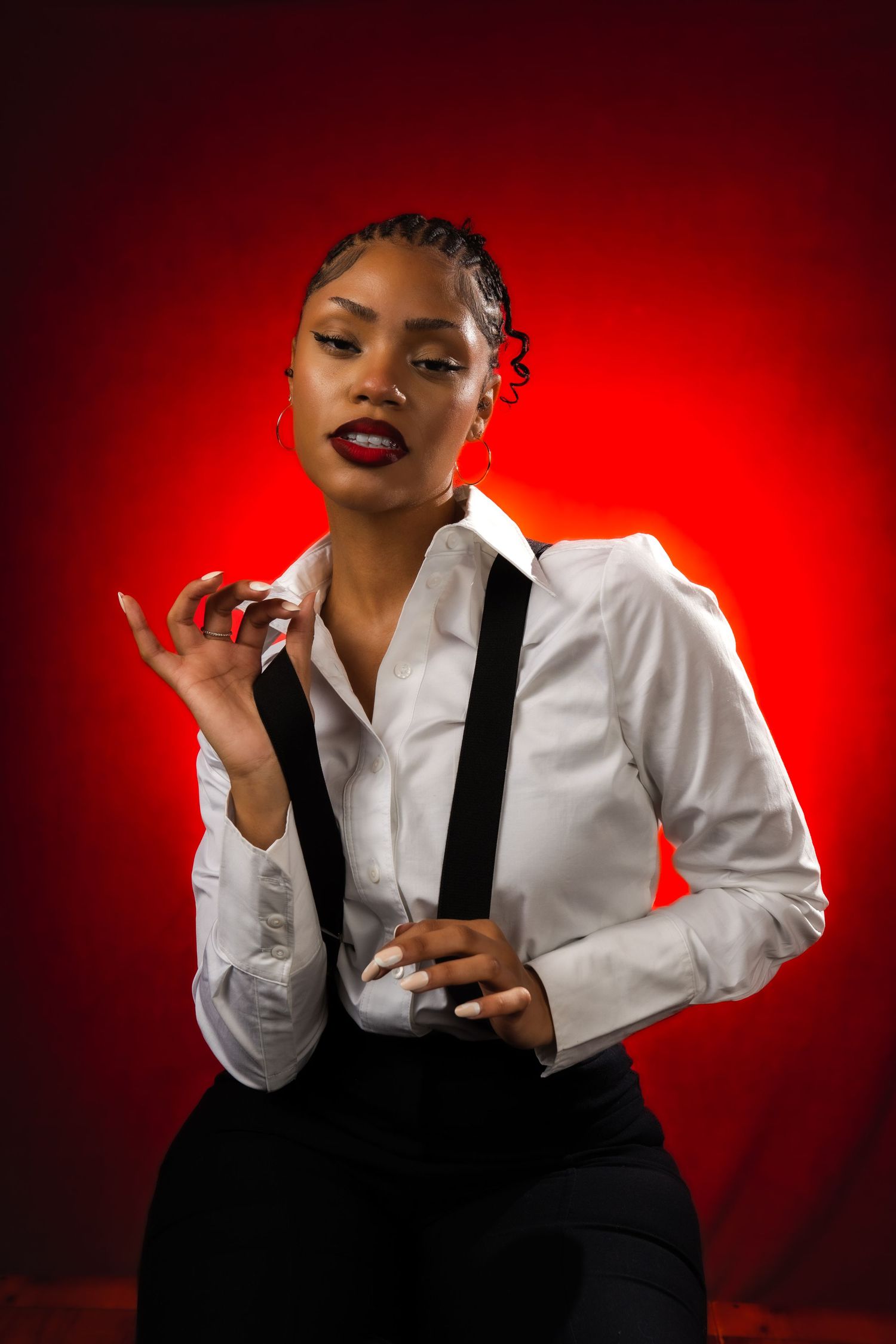 A figure in a white shirt and black suspenders poses dramatically against a red backdrop with dramatic lighting effects.