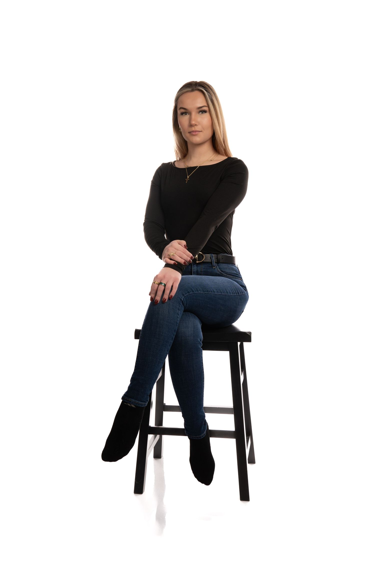 Woman in black top and jeans sits on dark wooden stool in four different poses against white background.
