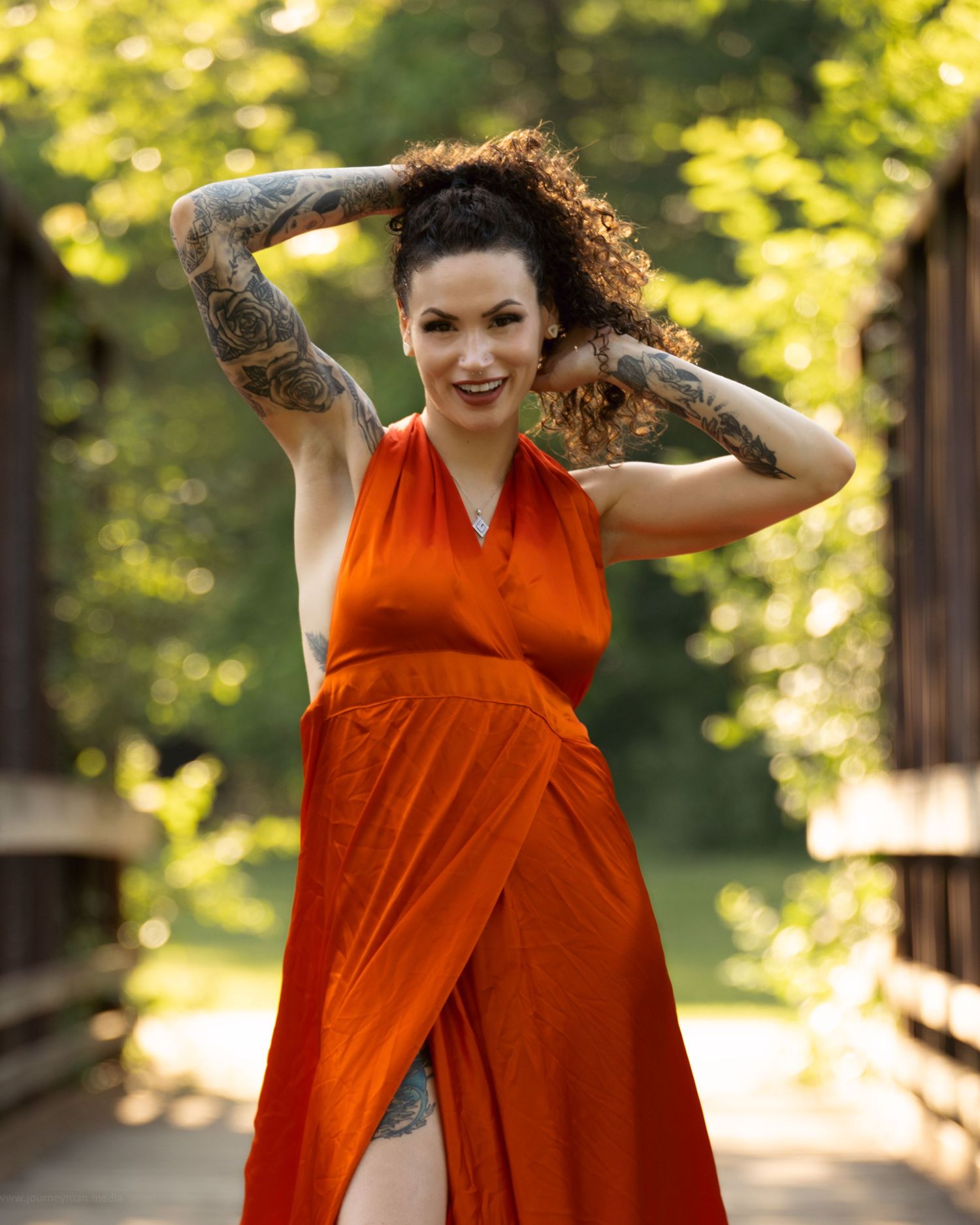 Person in flowing orange dress twirls joyfully in a sunlit garden setting with greenery in the background.