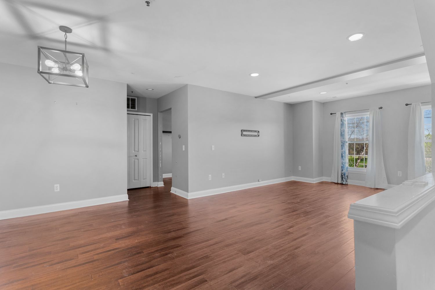 Open concept living space with hardwood floors, white walls, and natural lighting from windows.