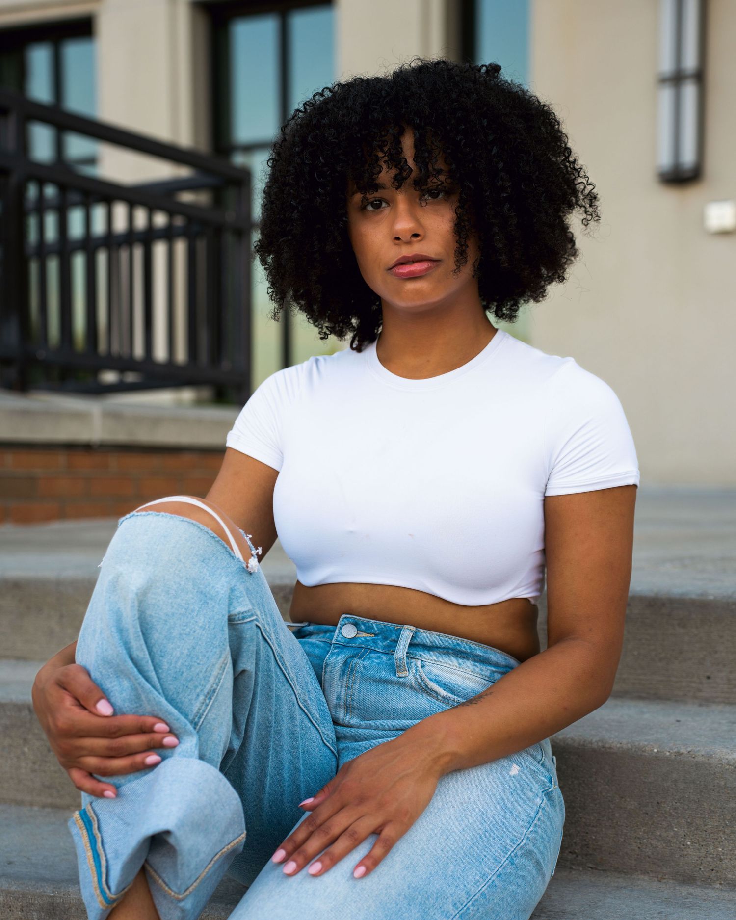 Person wearing white t-shirt and light denim jeans sits casually in outdoor urban setting.