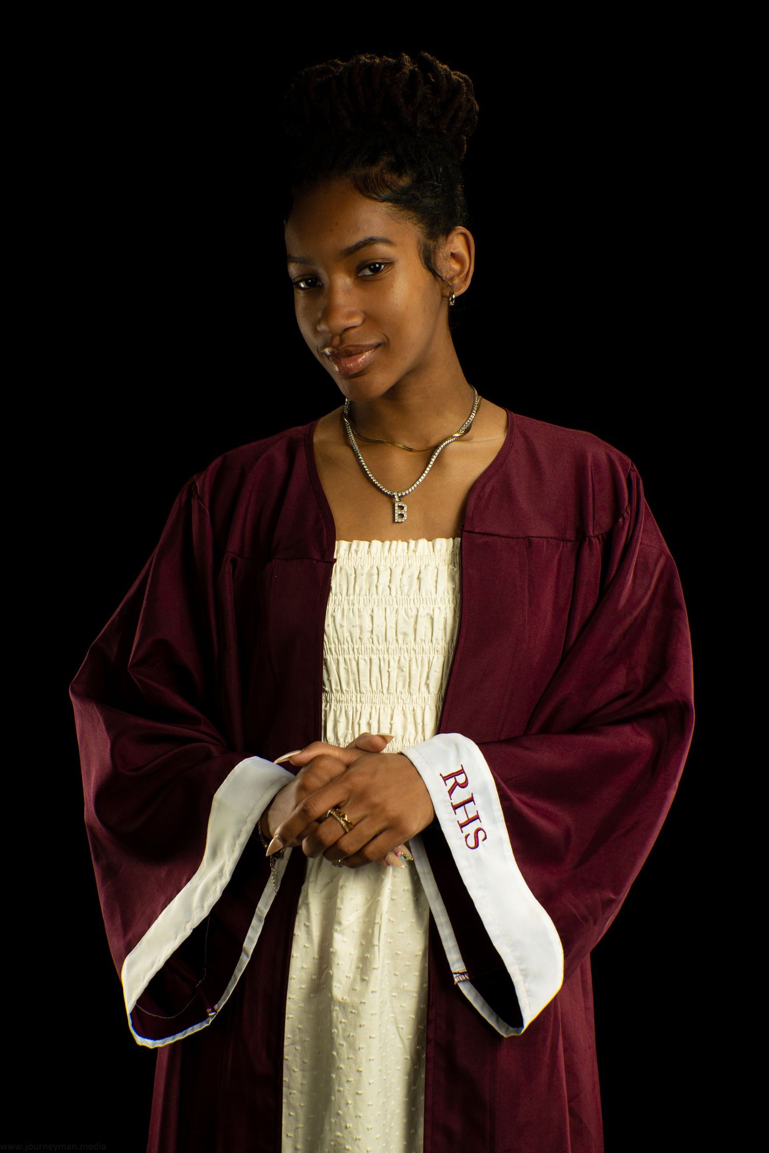A person wearing a burgundy graduation gown and white dress poses against a black background.