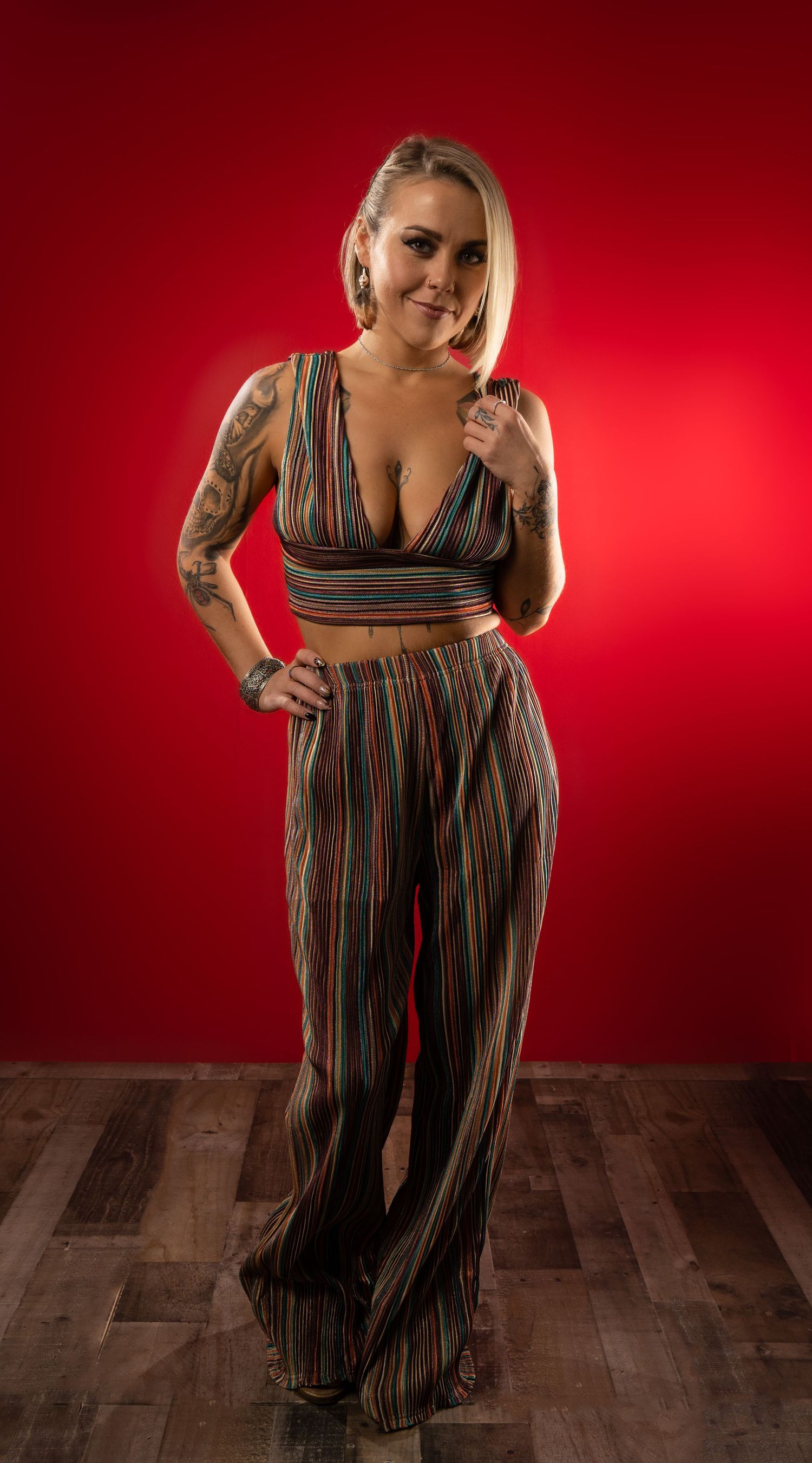 Fashion model in striped jumpsuit poses against red backdrop on wooden floor during professional photoshoot.