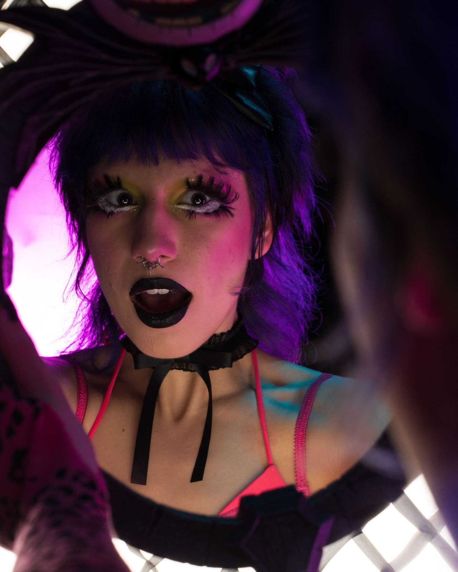 Dramatic portrait with purple lighting and bold makeup in a dark setting.