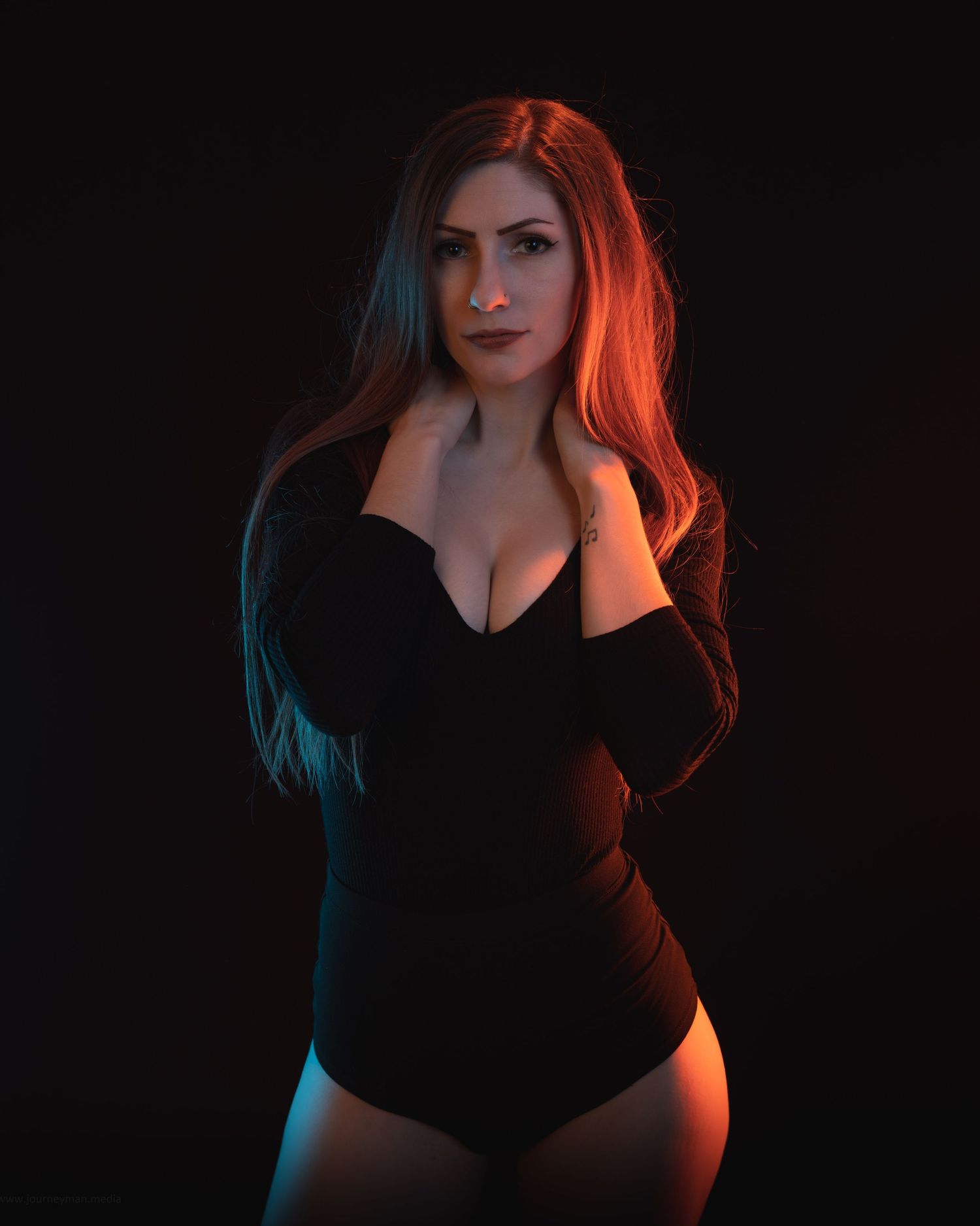 A woman in a black bodysuit poses against a dark background with dramatic red and blue lighting accents.